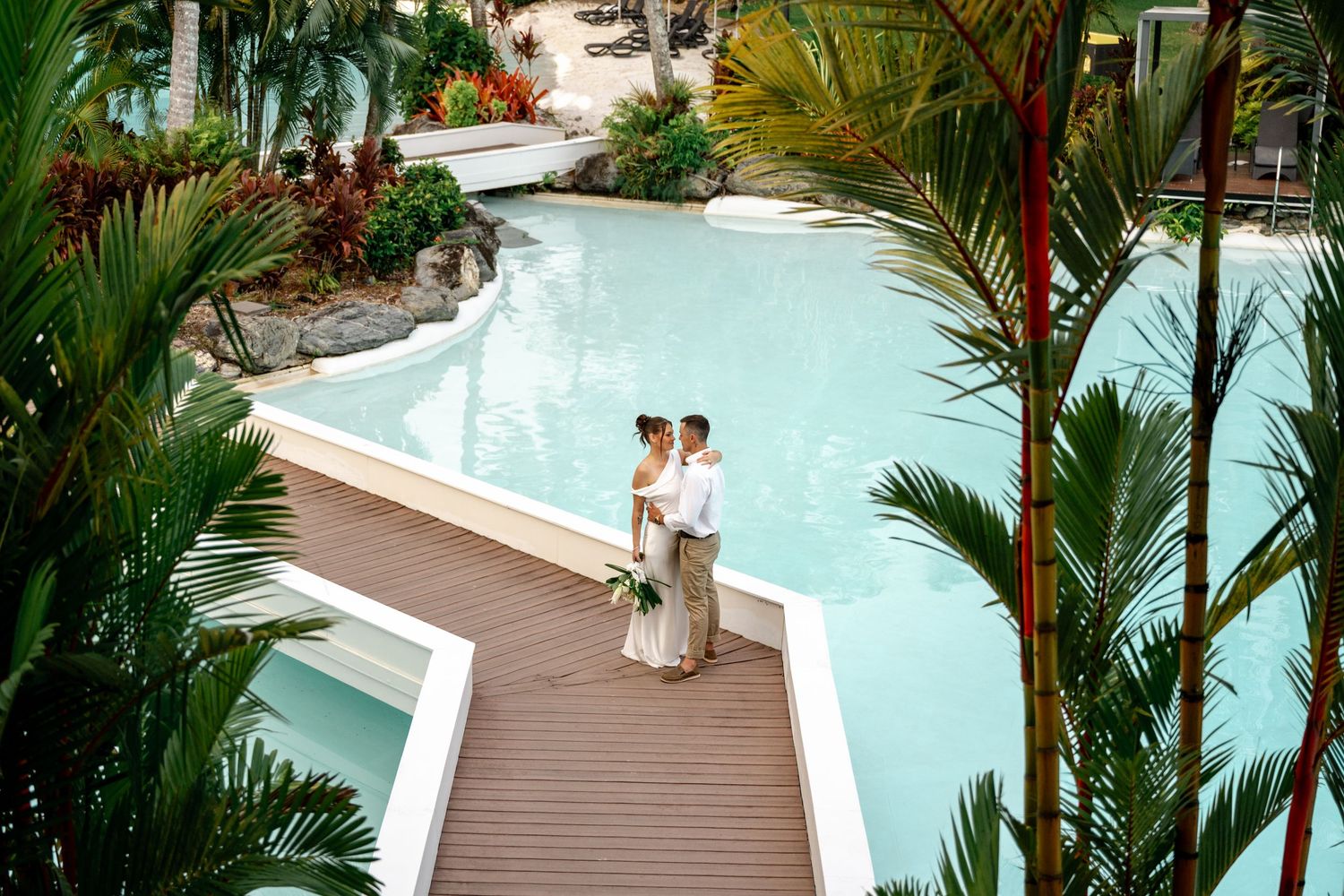 Aerial view of newlyweds embracing on a resort boardwalk surrounded by lush tropical gardens at Sheraton Grand Mirage Port Douglas.
