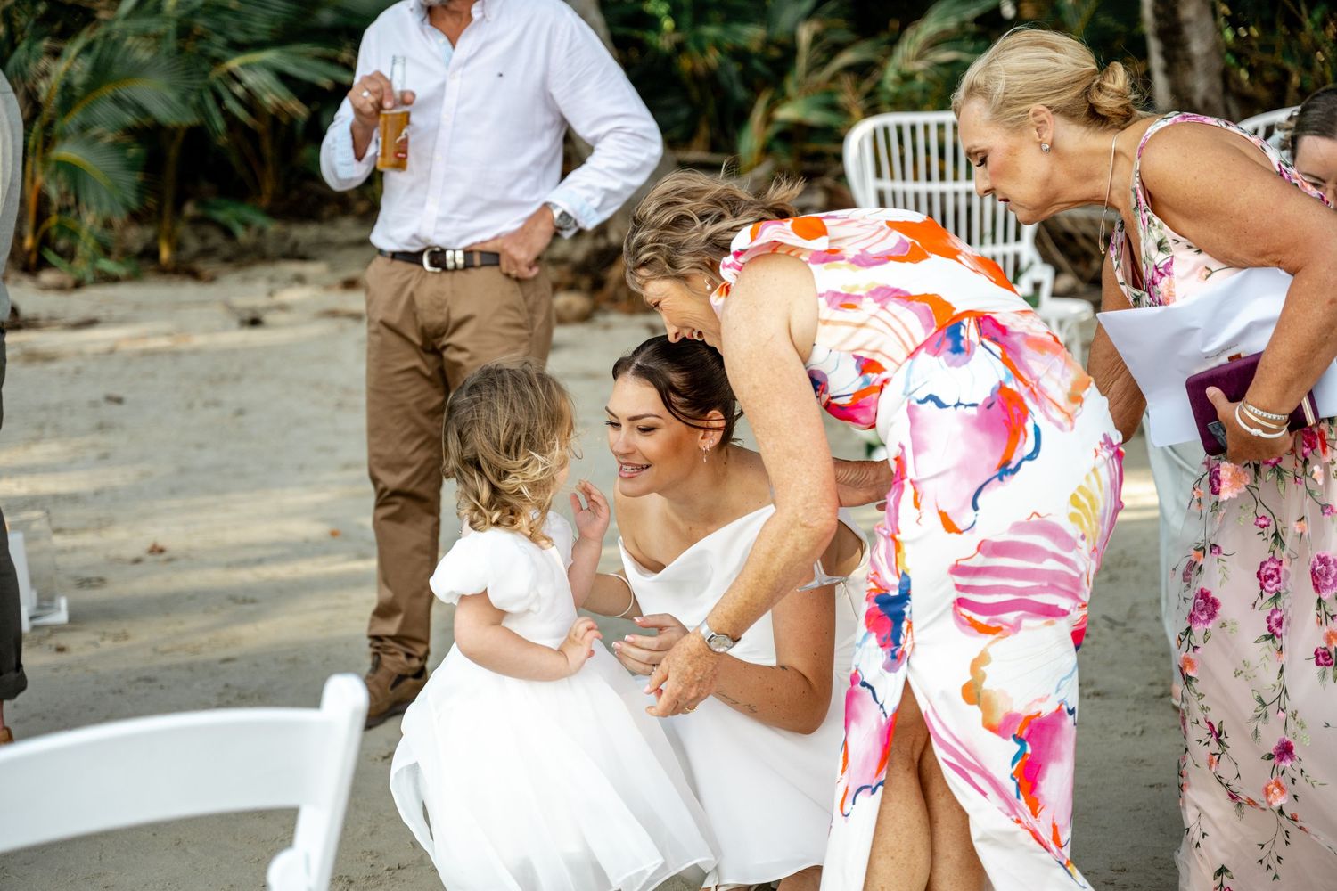 Bride in white gown kneeling to greet flower girl at tropical beach wedding at Four Mile Beach, Port Douglas.