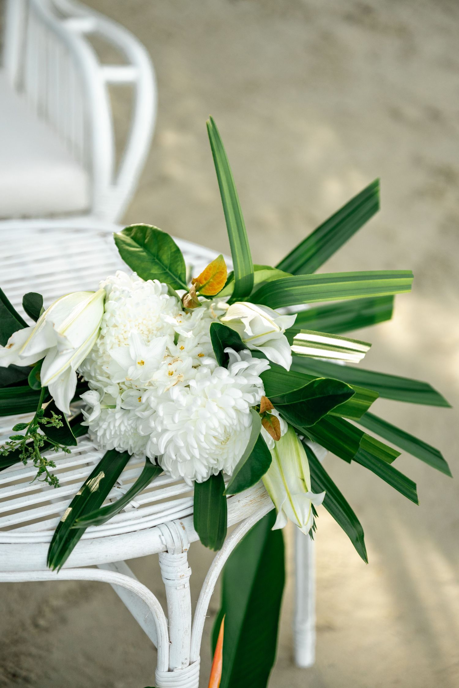White chrysanthemums and tropical green leaves bouquet on a white wicker chair at a beach wedding at Four Mile Beach, Port Douglas.