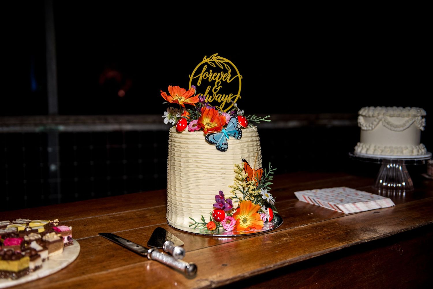 Wedding cake decorated with colorful flowers and forever always topper on wooden table.