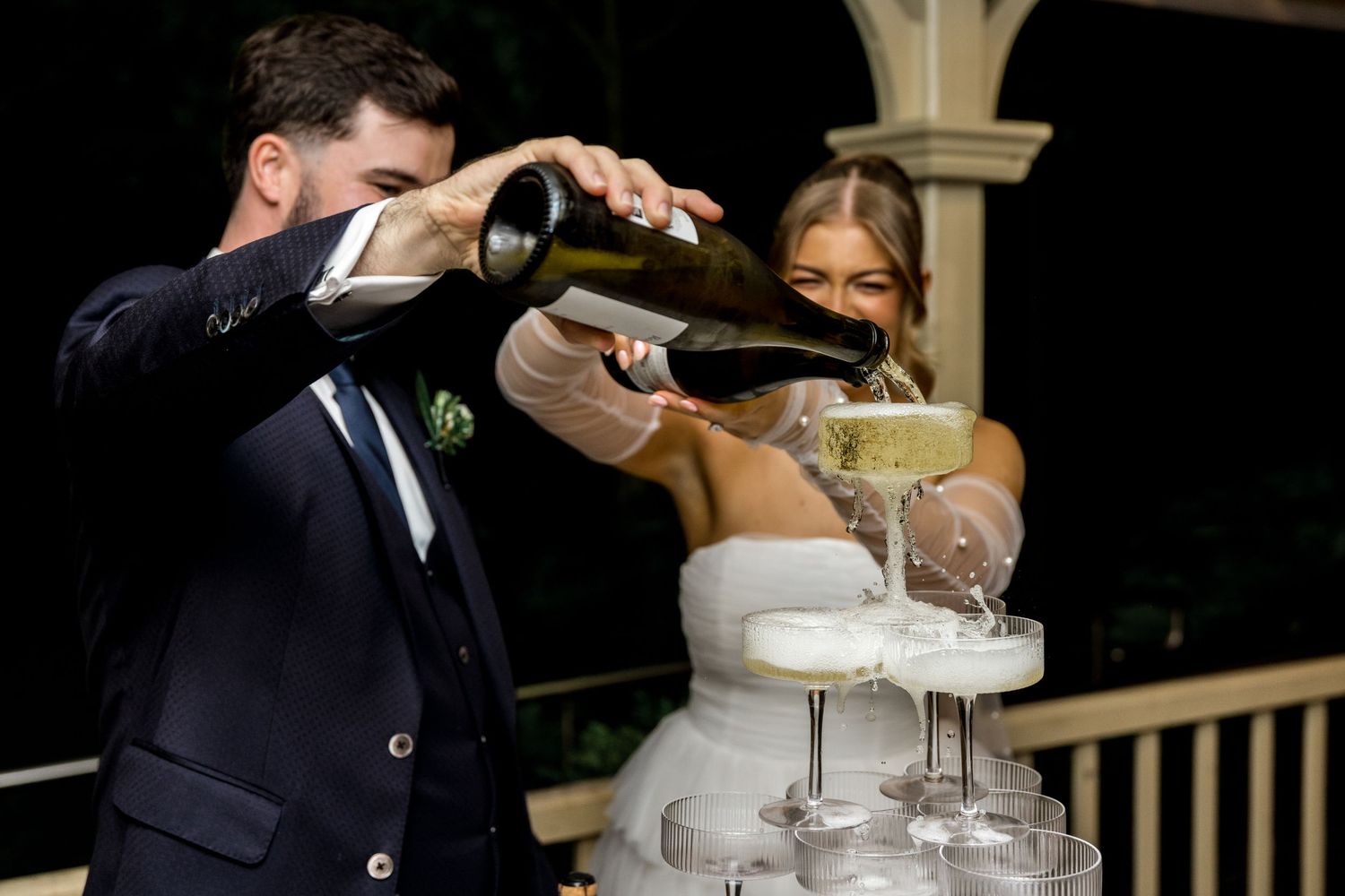 Bride and groom pour champagne together into a tiered champagne tower during their elegant wedding reception.