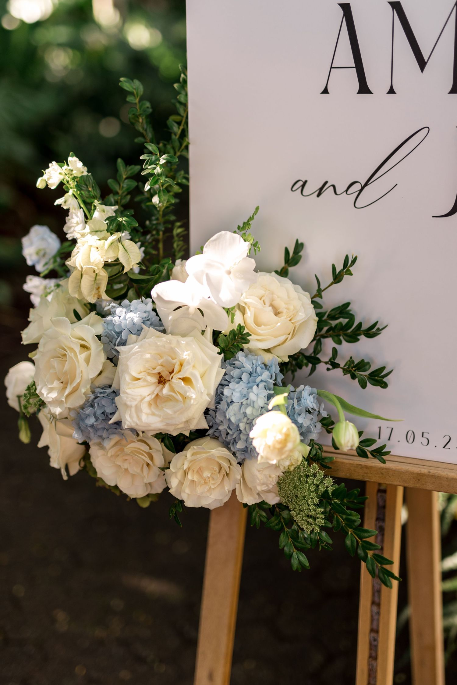 Close-up of wedding sign floral arrangement featuring white garden roses, blue hydrangeas, and green foliage.