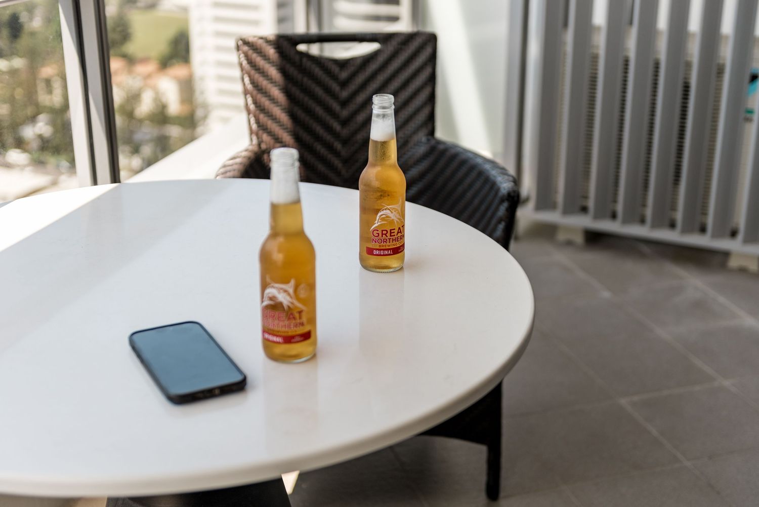 Two bottles of beer and a smartphone on a white round table on a balcony.
