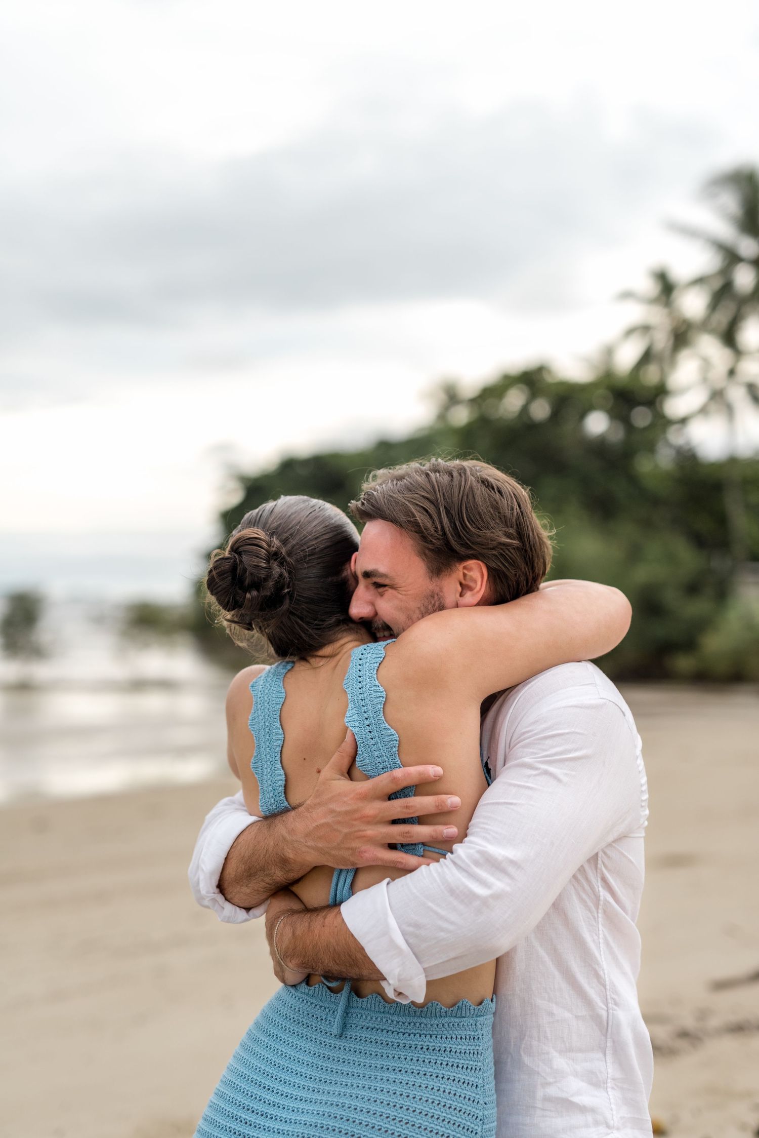 Close-up of joyful couple sharing warm embrace on tropical beach after marriage proposal.