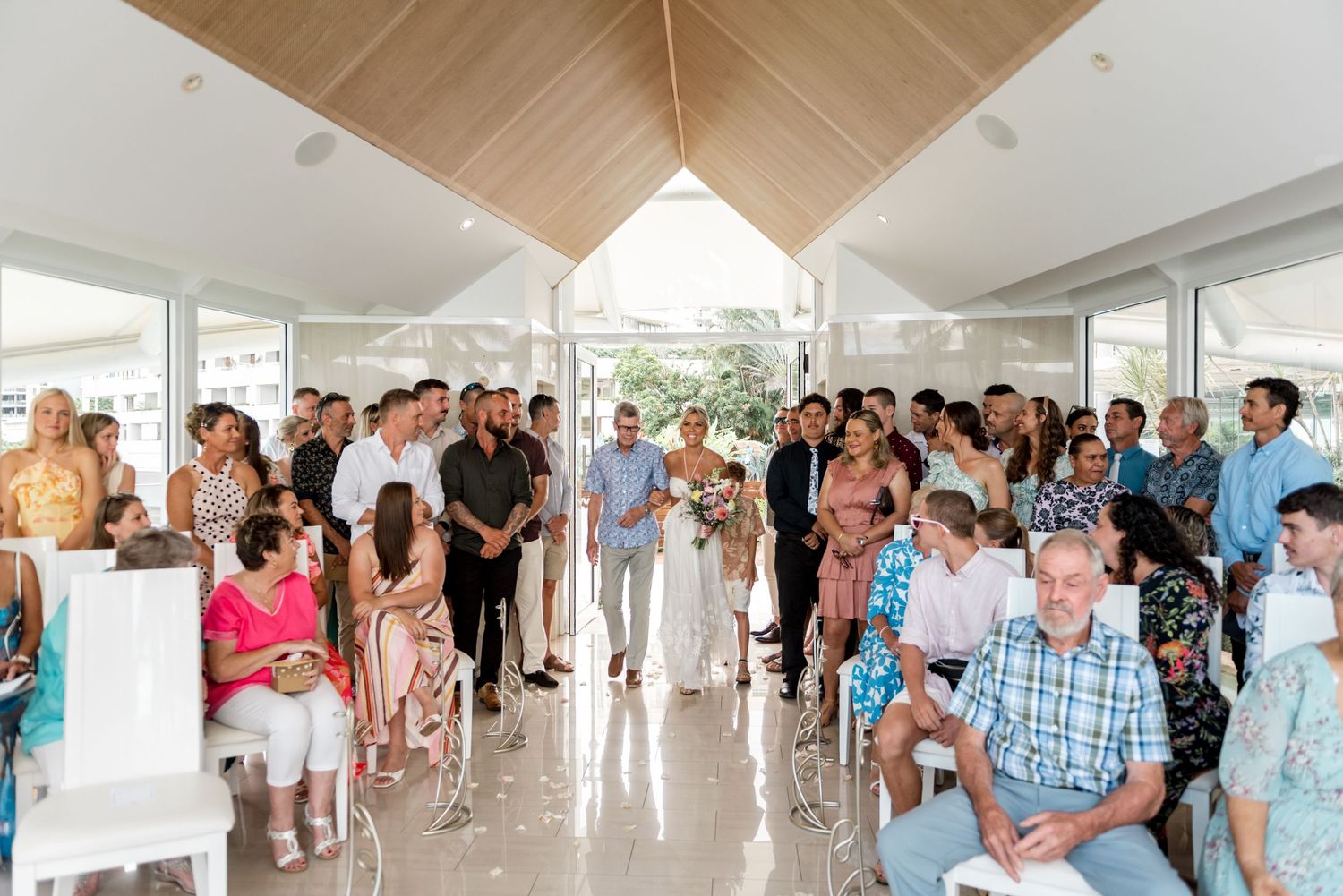Bride walking down the aisle in a bright modern chapel surrounded by guests.