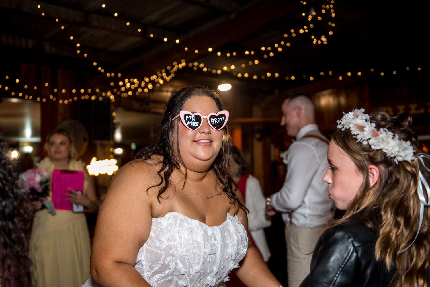 Bride wearing fun heart-shaped novelty sunglasses dancing at her wedding reception celebration.