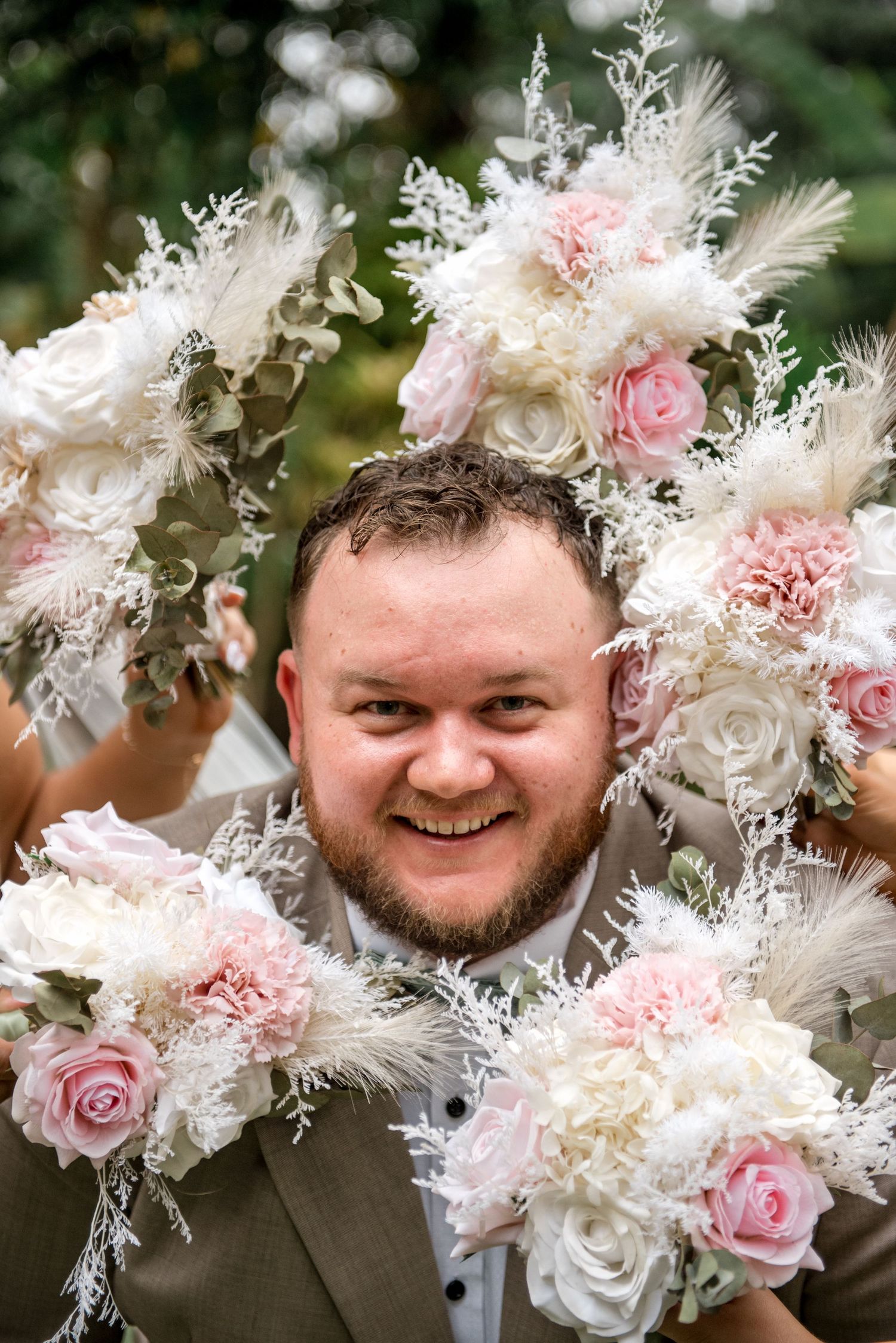 Smiling groom surrounded by pink and white floral bouquets creating a beautiful frame around his face.