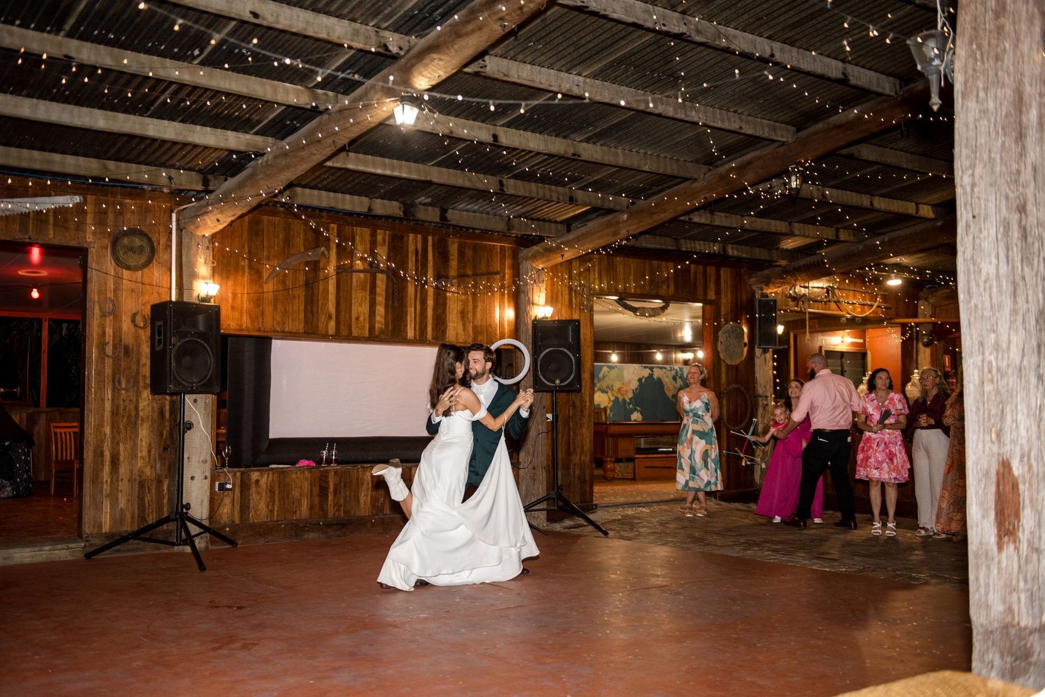 Bride and groom share a romantic dip during their first dance in a barn venue.