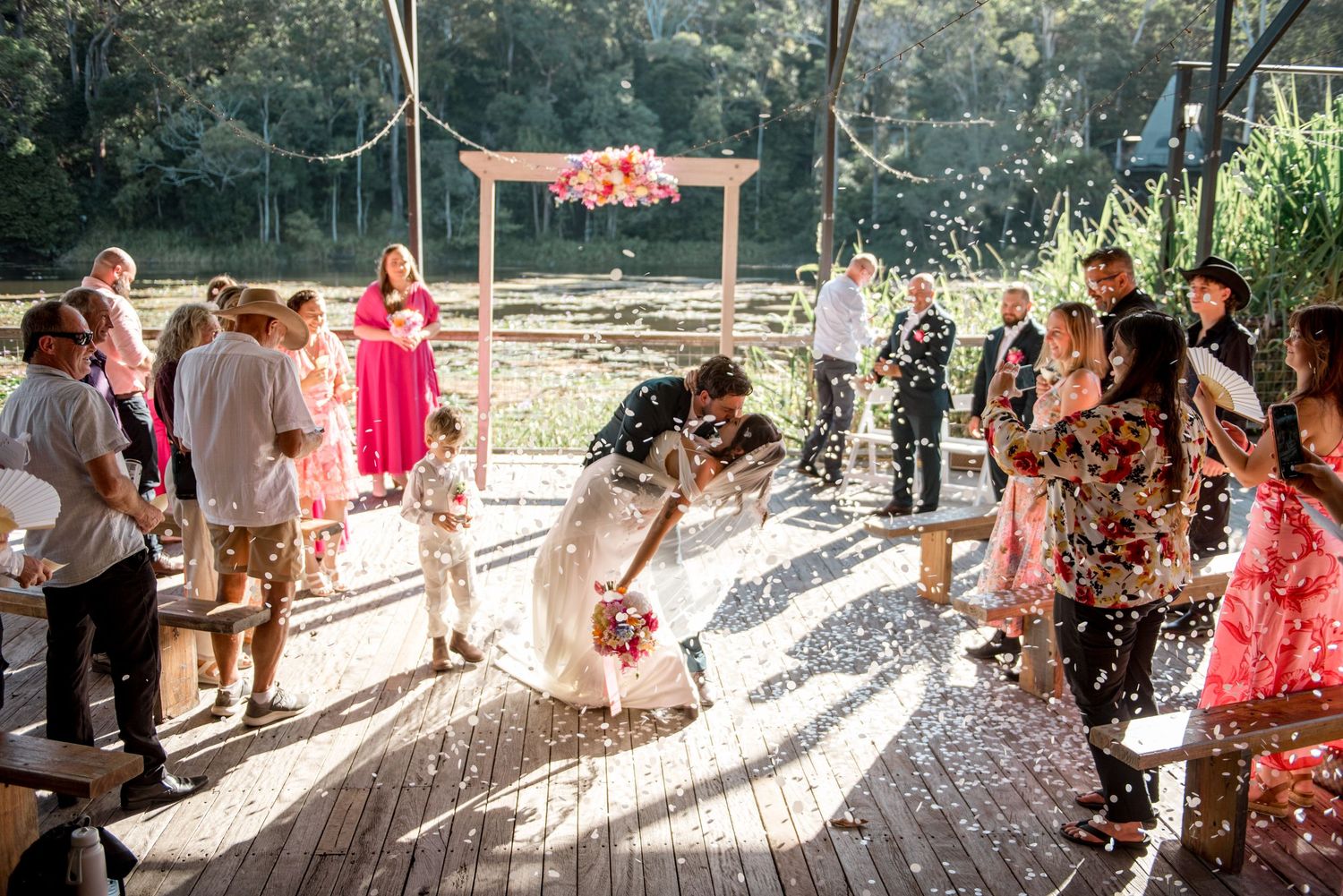 Couple kissing while guests throw confetti at outdoor wedding.