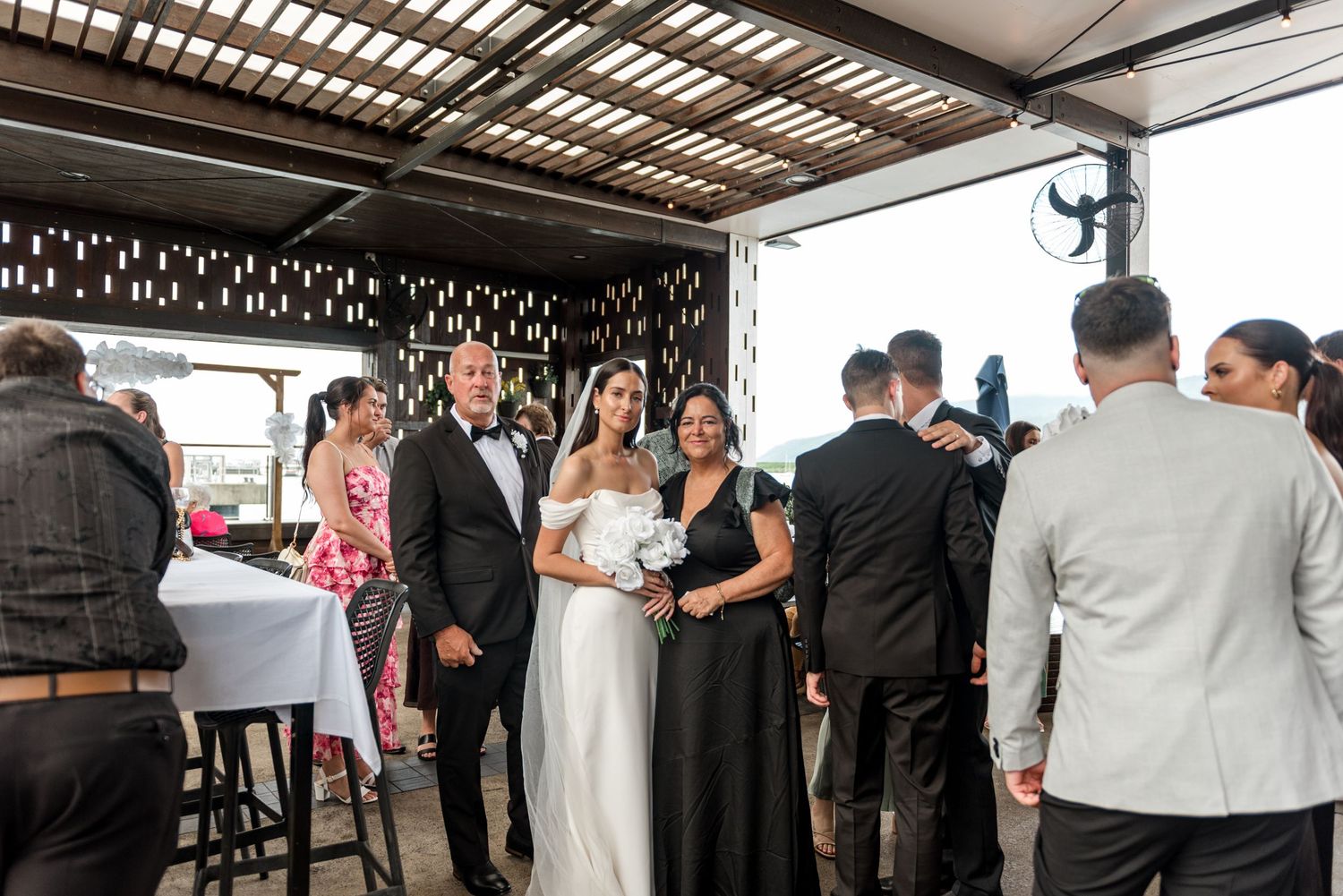 Bride in white off-shoulder gown posing with guests after outdoor rooftop wedding ceremony.