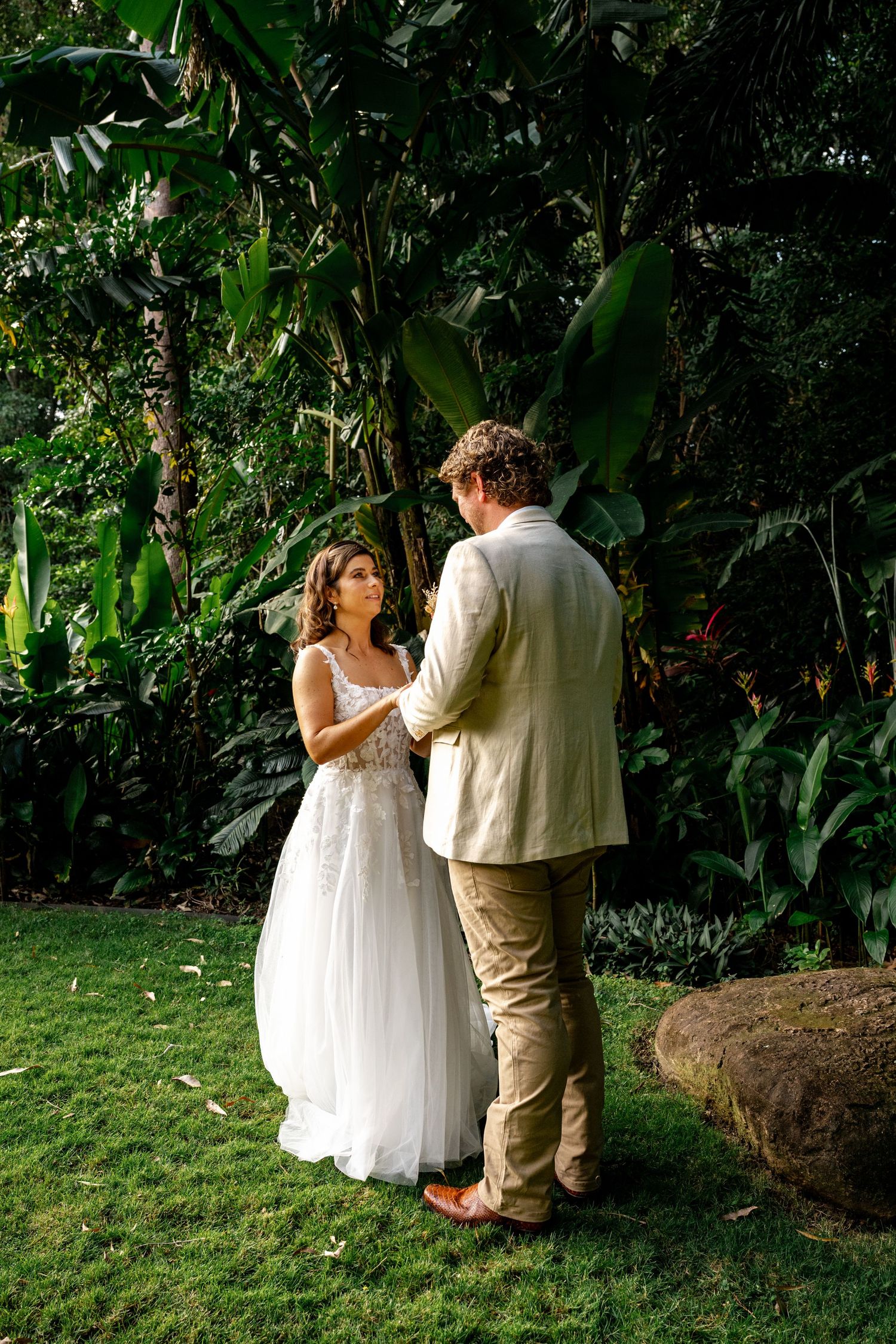 A bride and groom hold hands during their intimate outdoor wedding ceremony in a tropical garden.