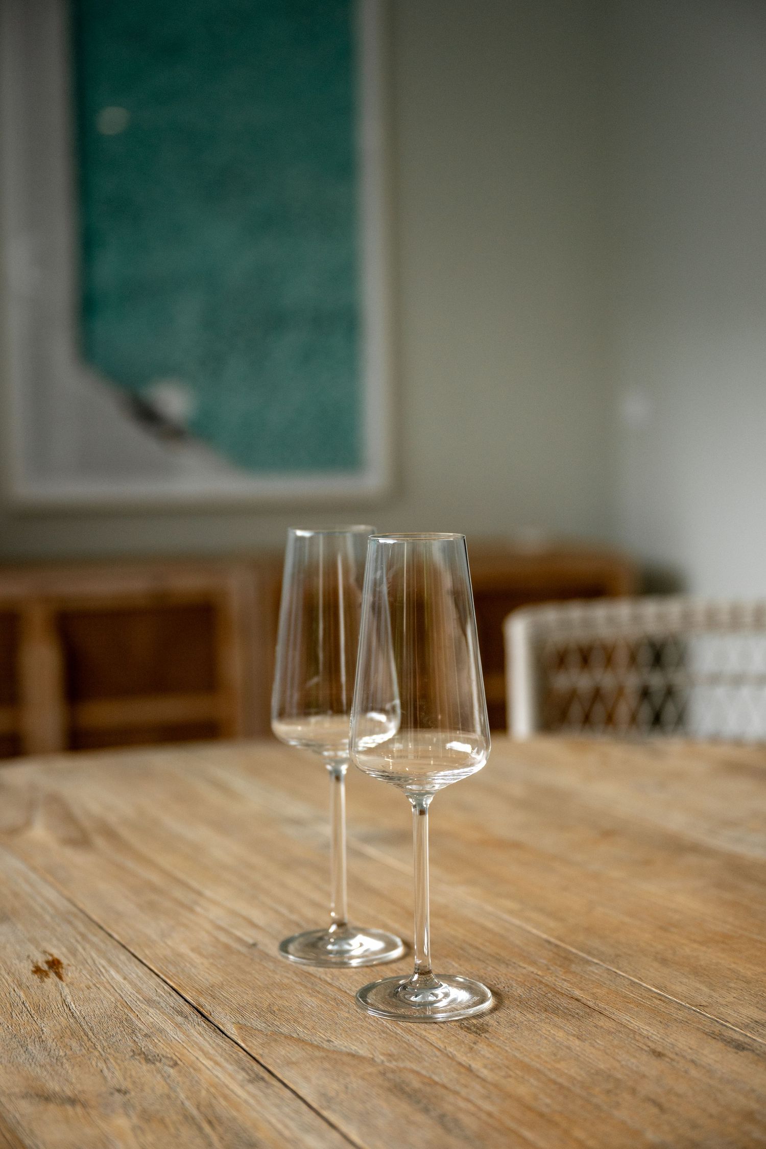 Two empty crystal champagne flute glasses on a rustic wooden table with blurred interior background.