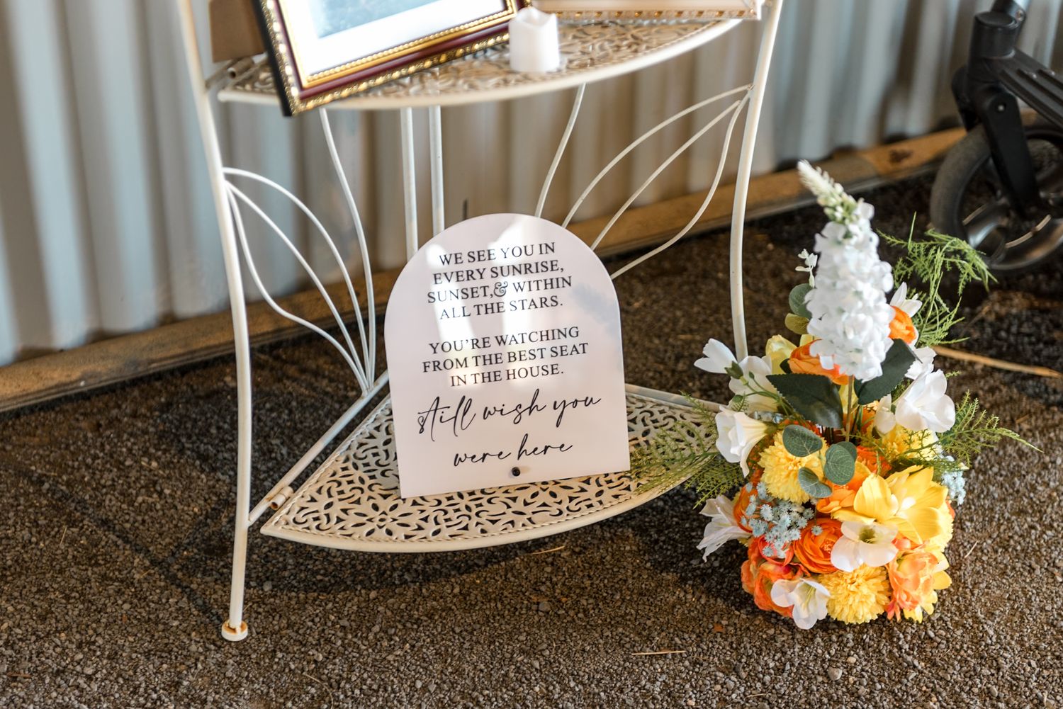 Memorial wedding sign on ornate white stand reading still wish you were here with floral bouquet.