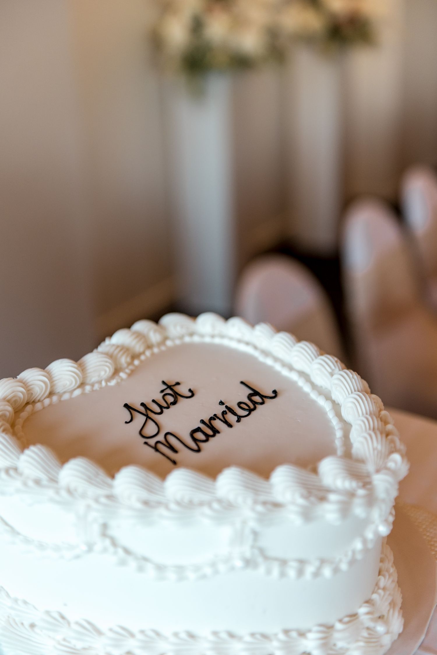Overhead view of a heart-shaped white wedding cake with Just Married script and decorative piped borders.