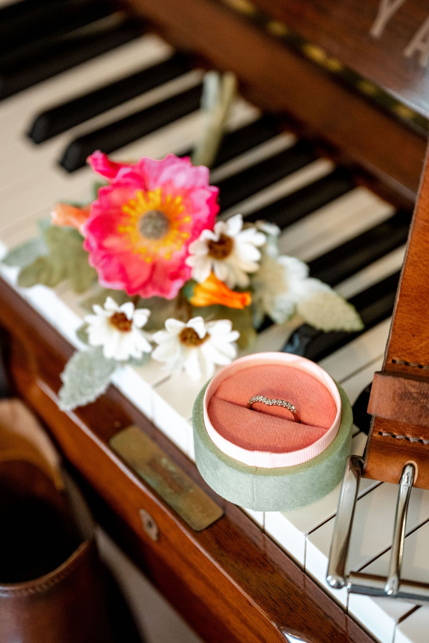 Gold wedding ring in pink velvet box displayed on piano keys with colorful flowers.