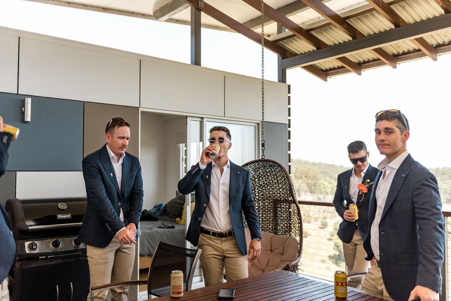 Group of groomsmen in suits drinking and celebrating together on an outdoor patio.