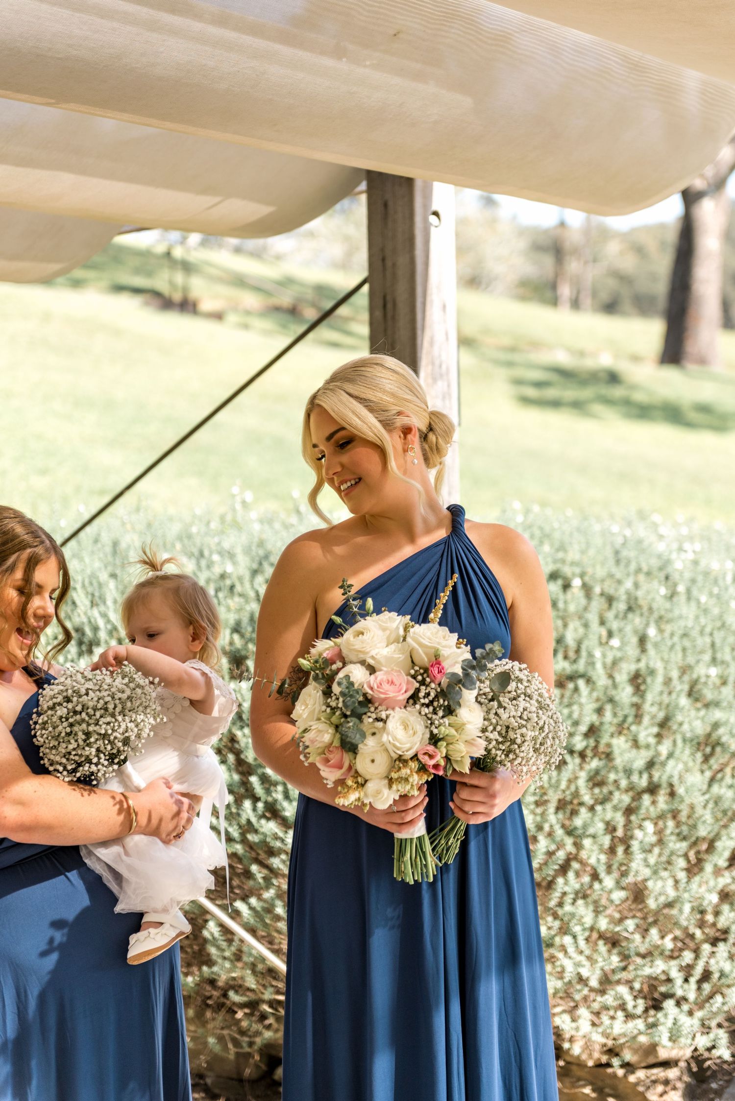 Smiling bridesmaid in blue dress holds a bouquet of roses and baby's breath at a wedding.
