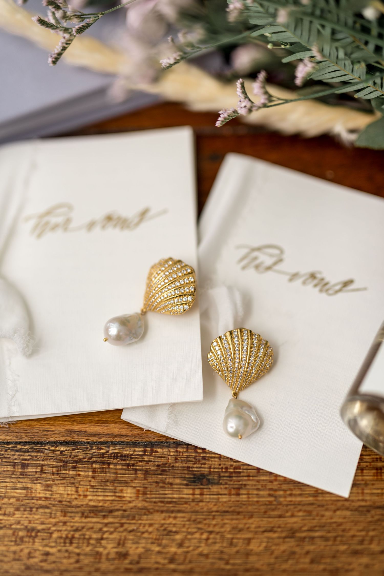 Two gold seashell drop earrings with baroque pearls displayed on white cards with calligraphy.