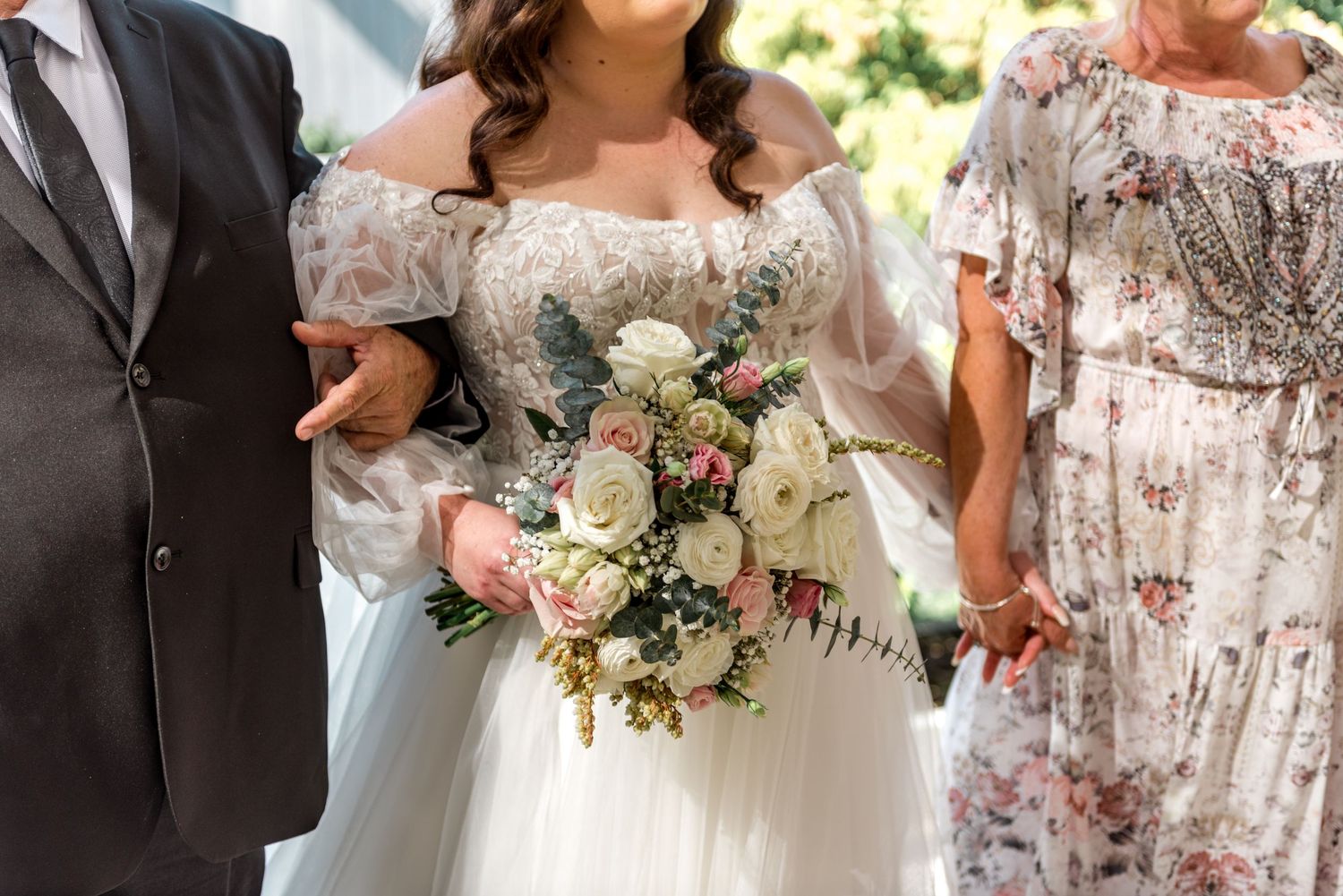 Bride holds a beautiful bouquet of white and pink roses in an off-shoulder wedding gown.