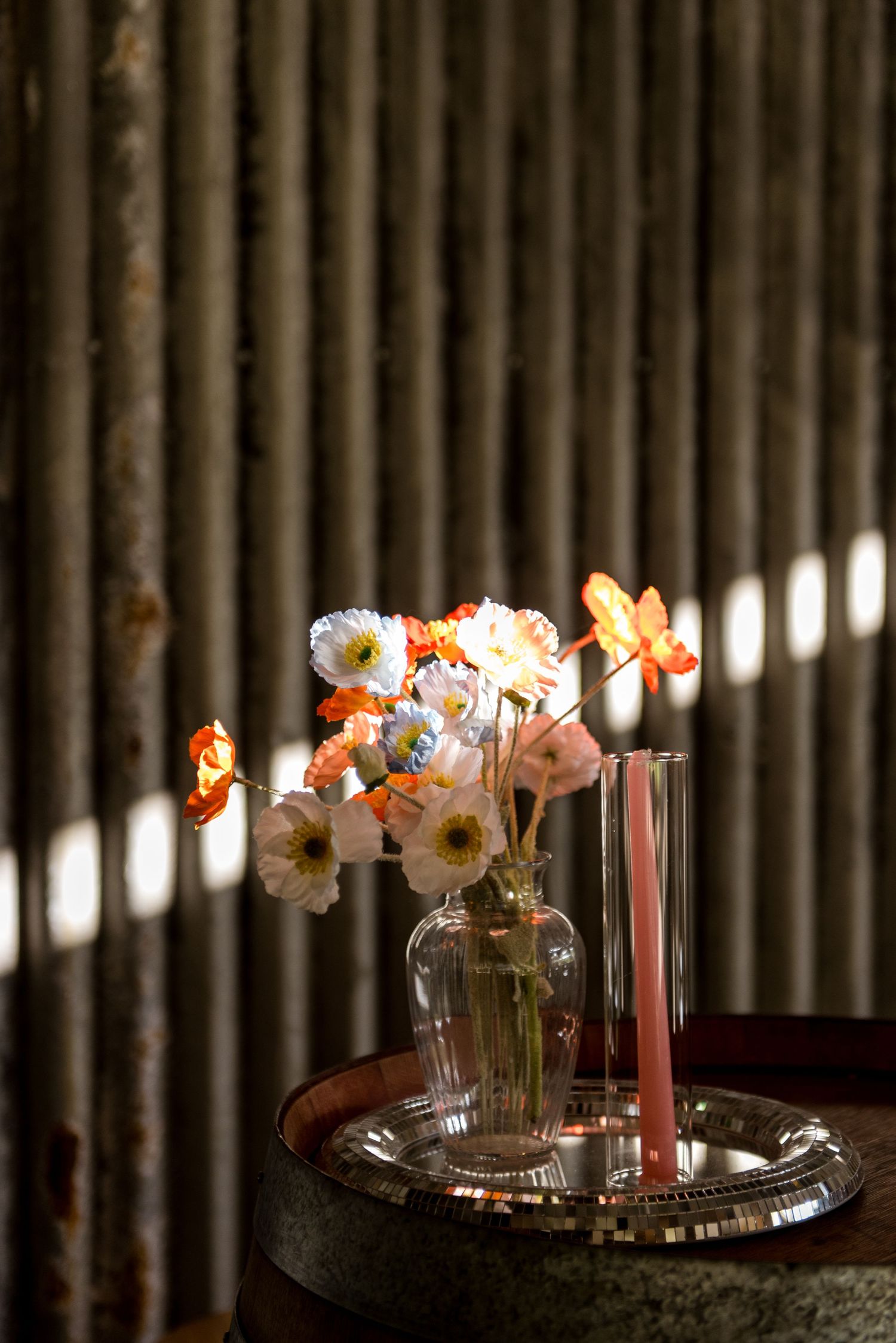 Delicate peach and white poppy floral arrangement in glass vase with pink candles on silver tray.
