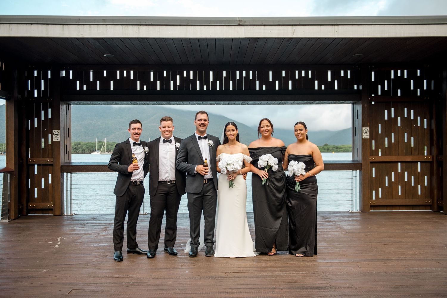 Bridal party posing in black and white formal wear at elegant waterfront venue.
