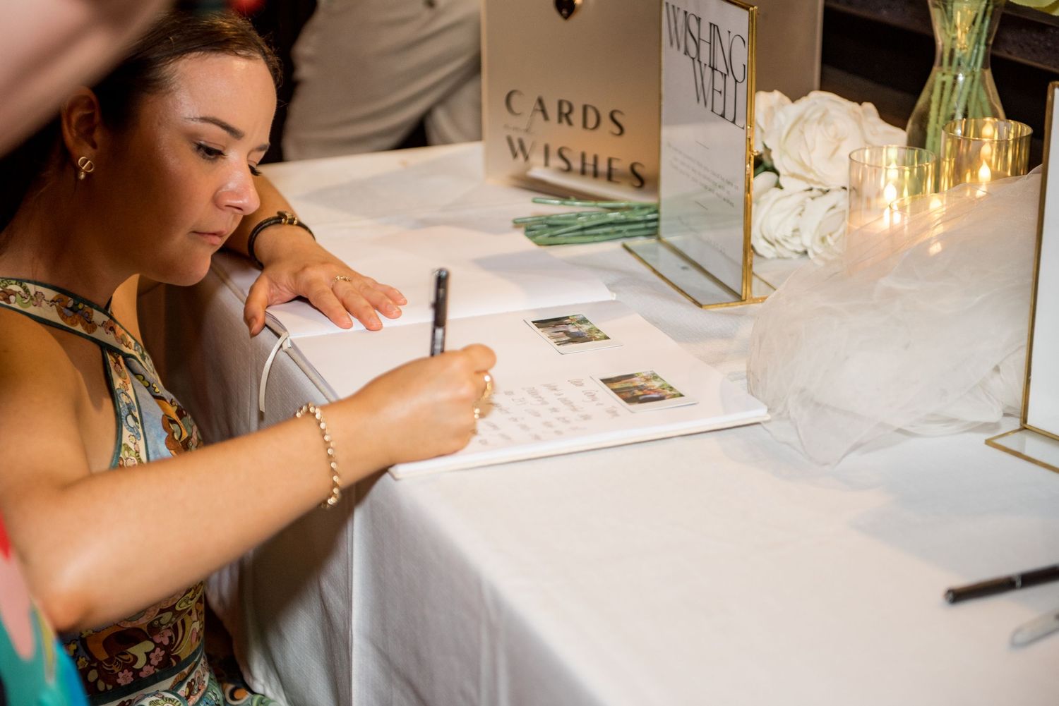 Wedding guest signs the guestbook at a decorated cards and wishes table at a reception.