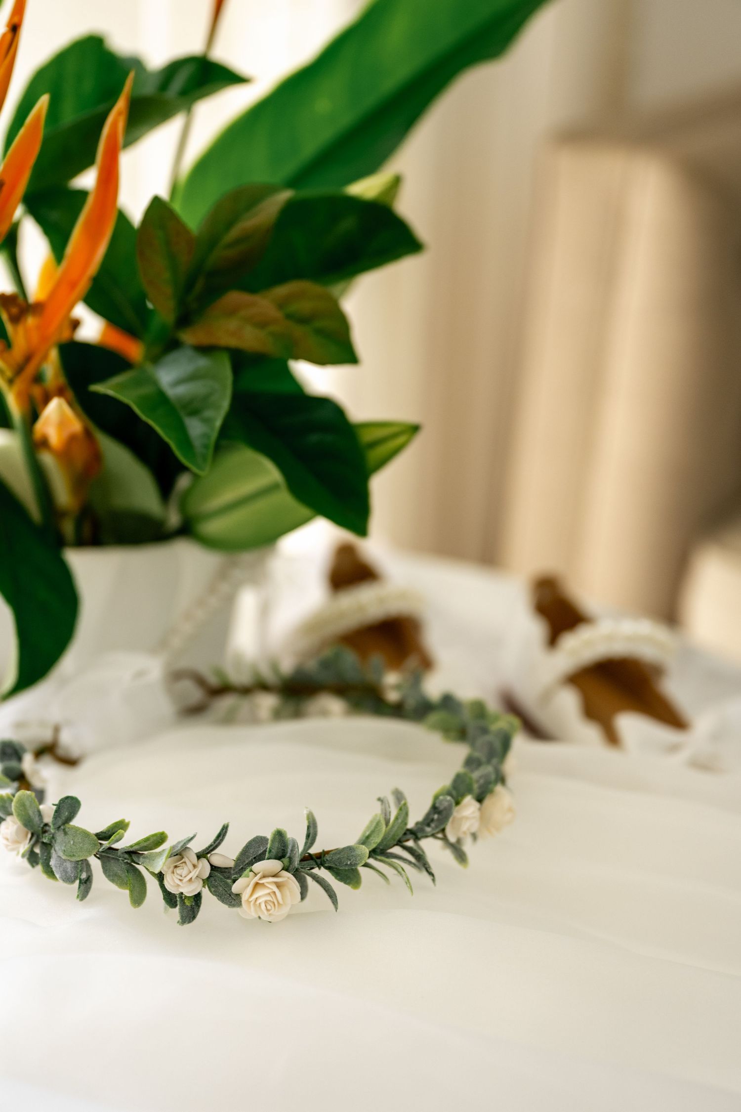 Eucalyptus and white rose bridal flower crown on white surface with tropical greenery behind.