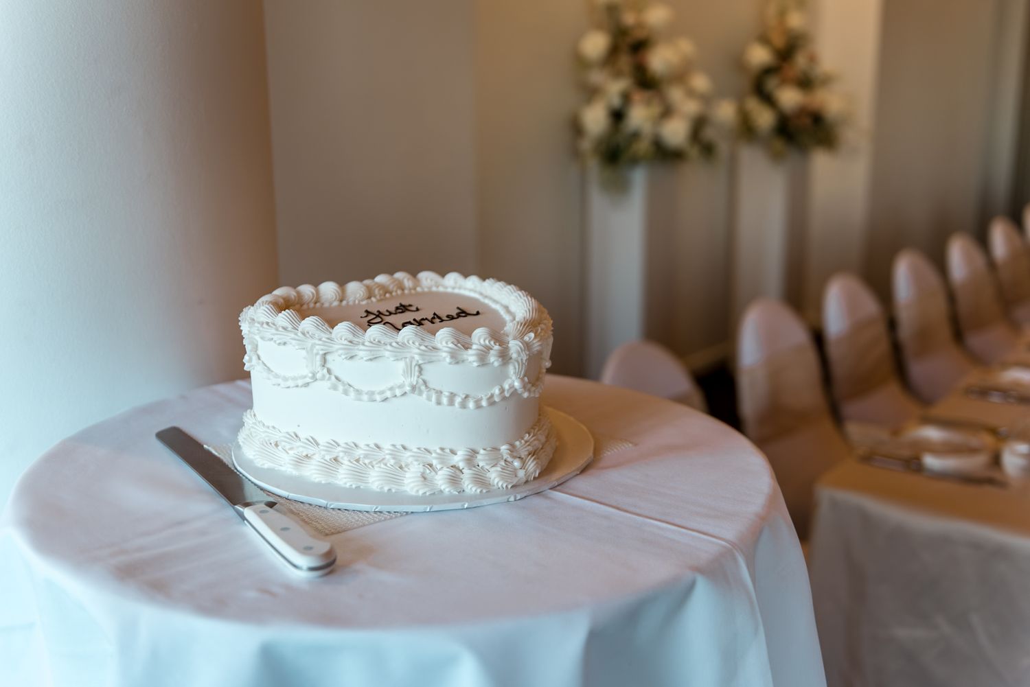 Elegant single-tier white wedding cake with pearl piping decorations on a draped table in a reception venue.