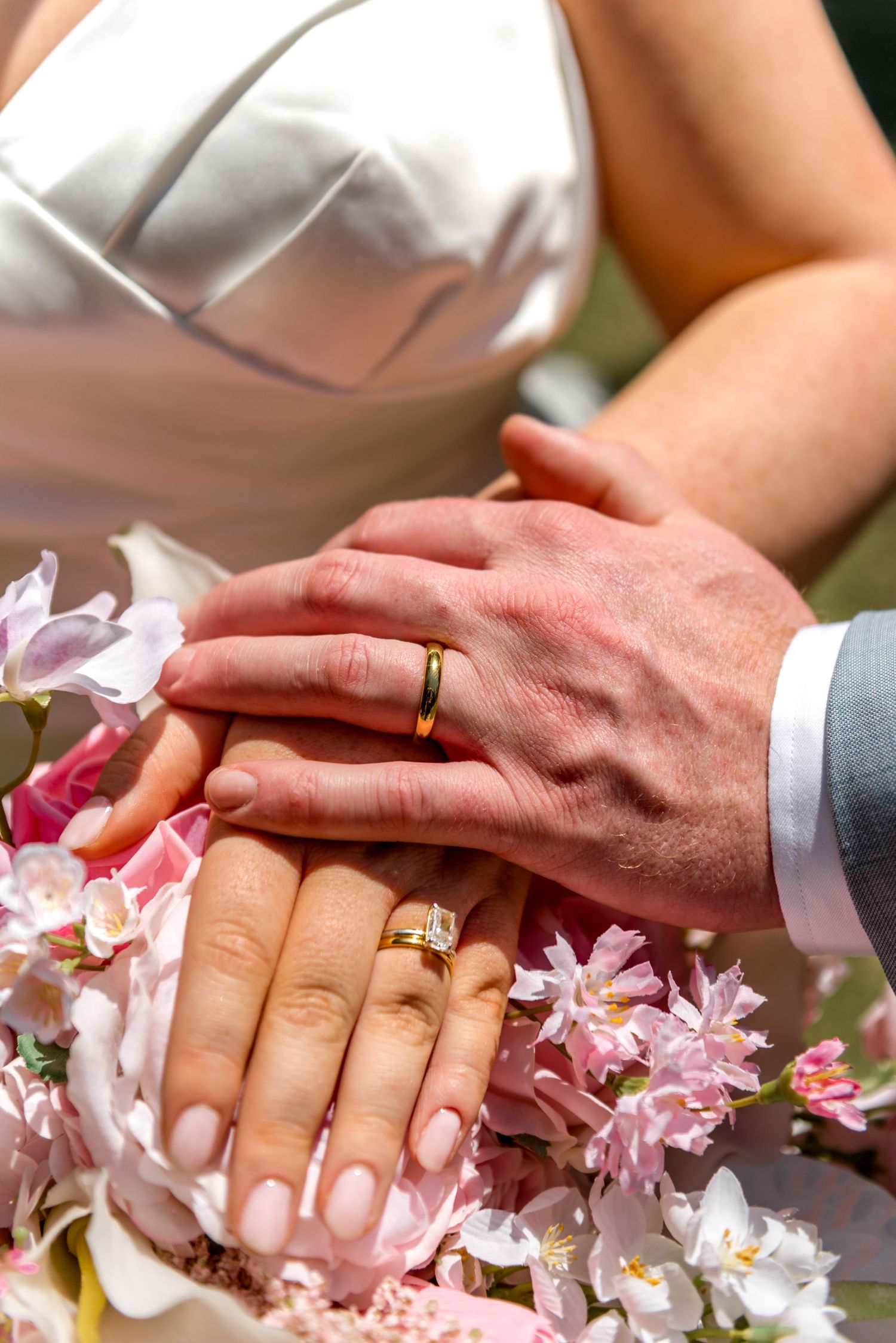 Newlyweds display their gold wedding rings resting on a beautiful pink and white floral bridal bouquet.