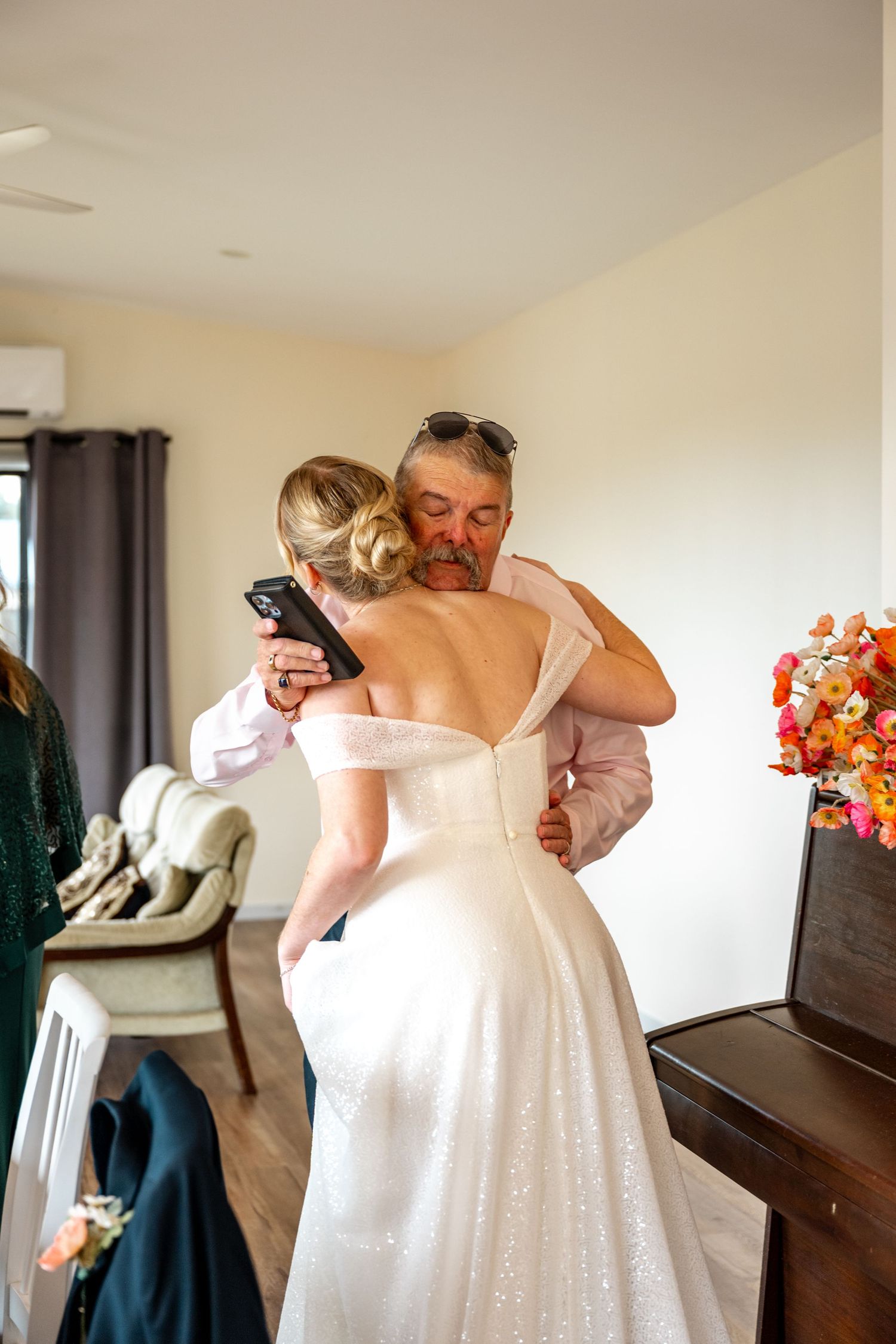 Father embraces his daughter in wedding dress during emotional bridal preparations at home.