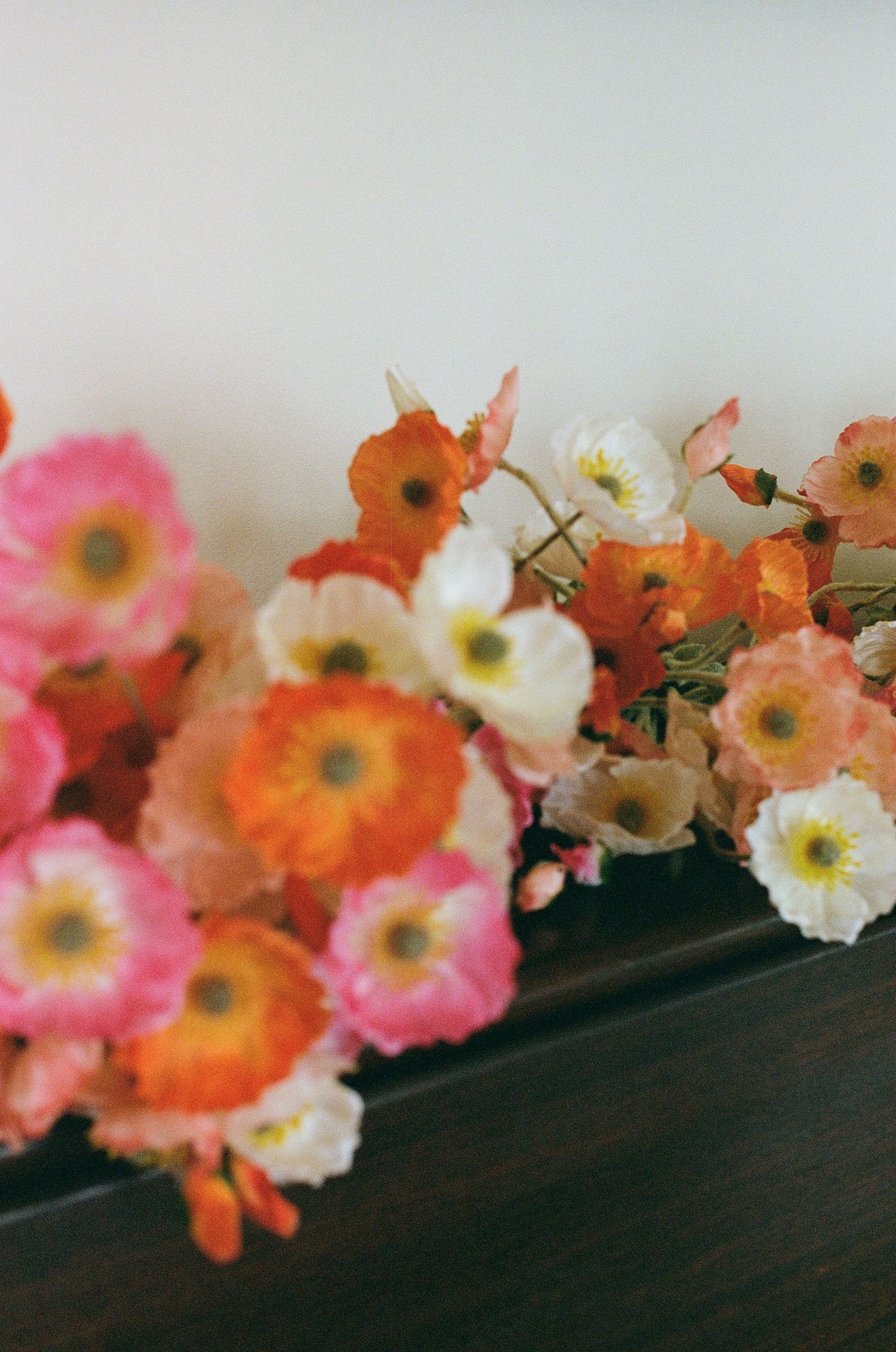 Colorful pink, orange, and white poppy flowers arranged on a dark wooden surface.