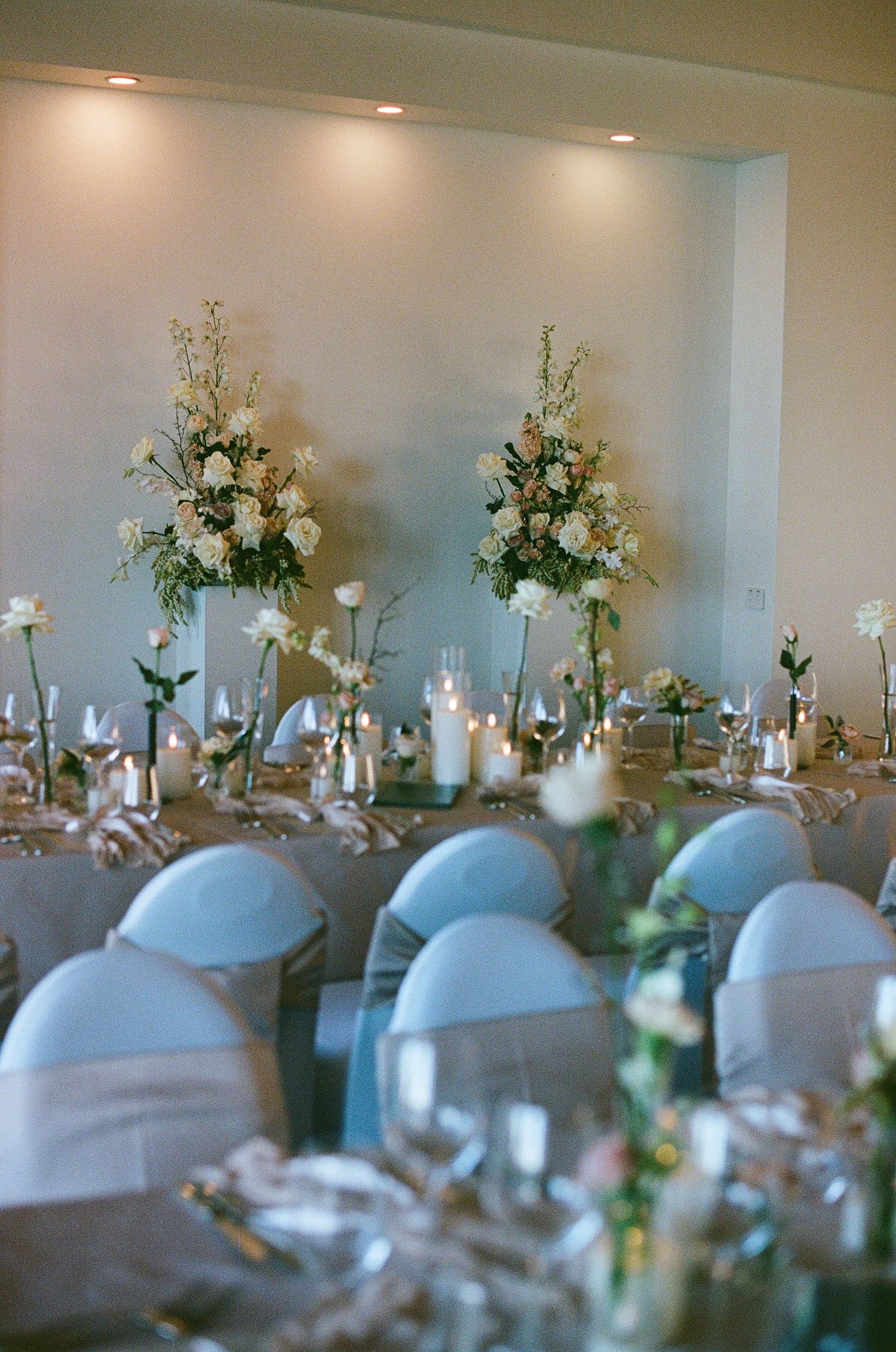 Elegant wedding reception tables with white floral centerpieces, candles, and light blue chair covers.