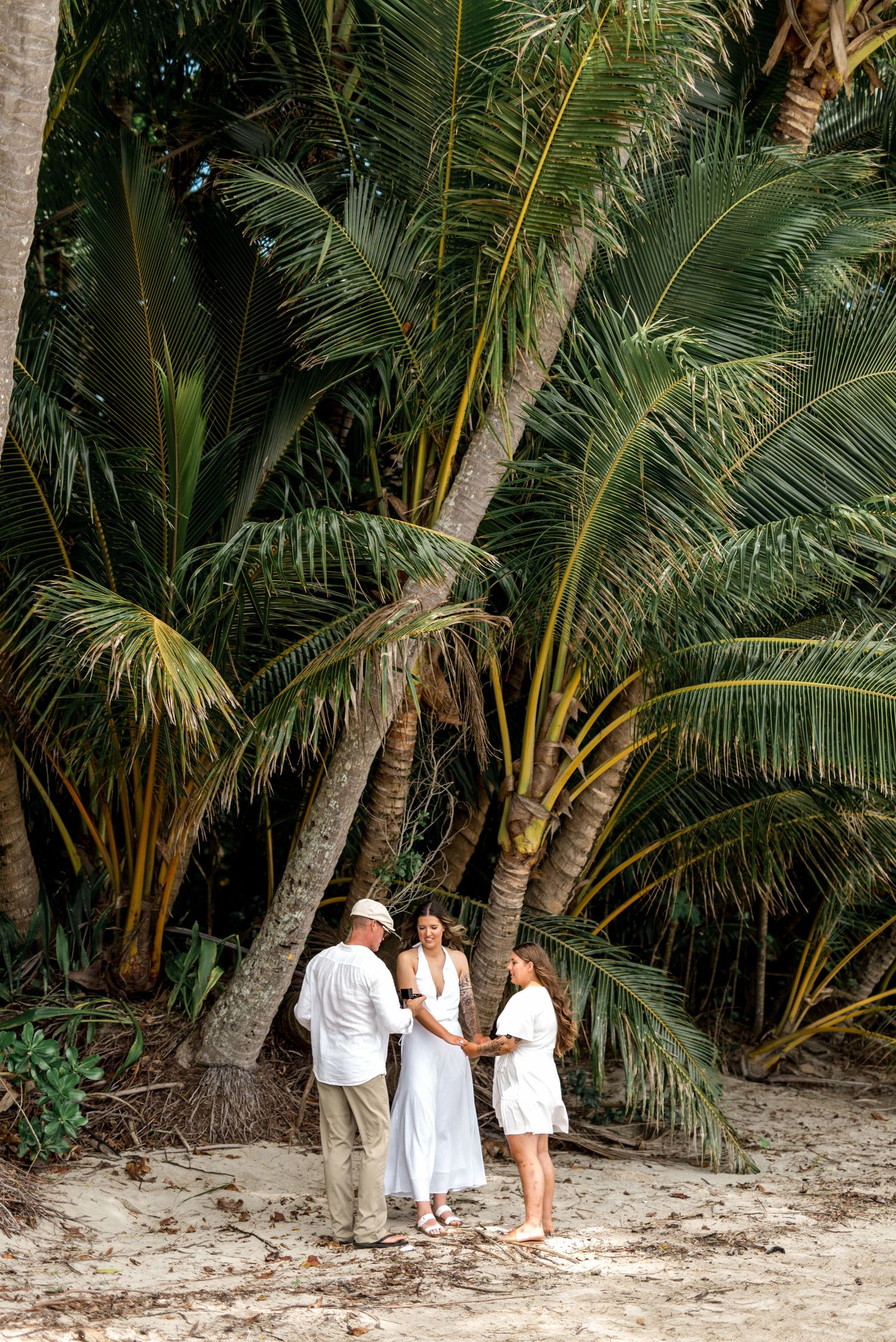 Couple exchanging vows in a small intimate beach ceremony surrounded by tropical palm trees.