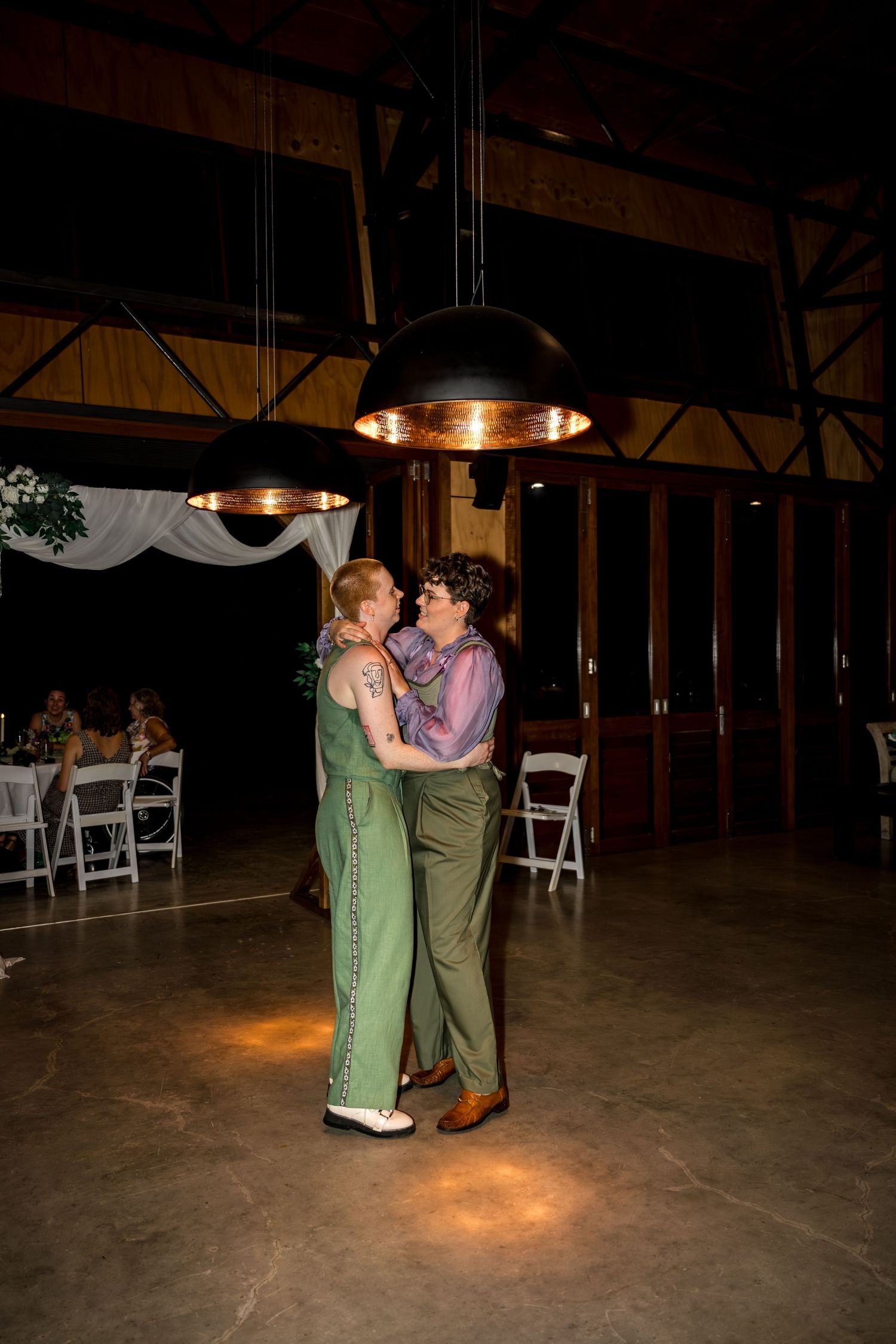 Newlywed couple sharing their first dance under warm pendant lights at wedding reception.