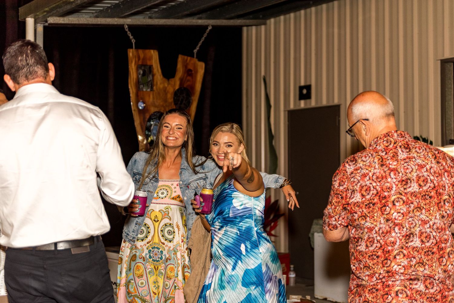 Guests socializing and dancing at an indoor evening event, wearing colorful tropical-patterned outfits.