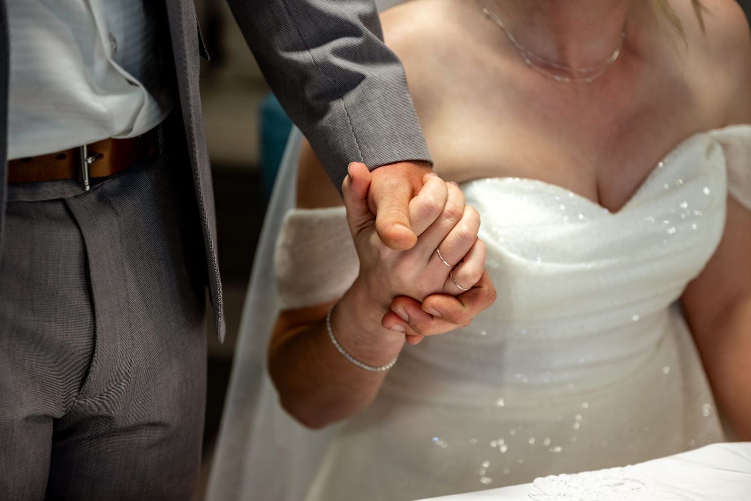 Close-up of bride and groom holding hands during wedding ceremony, bride wearing white gown.