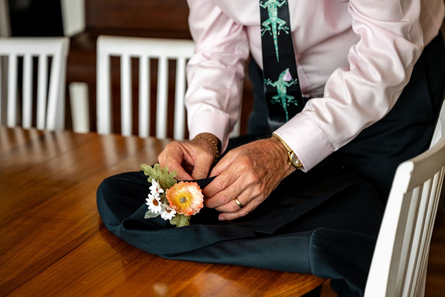 Close-up of mans hands arranging a floral boutonniere with orange and white flowers on dark fabric.
