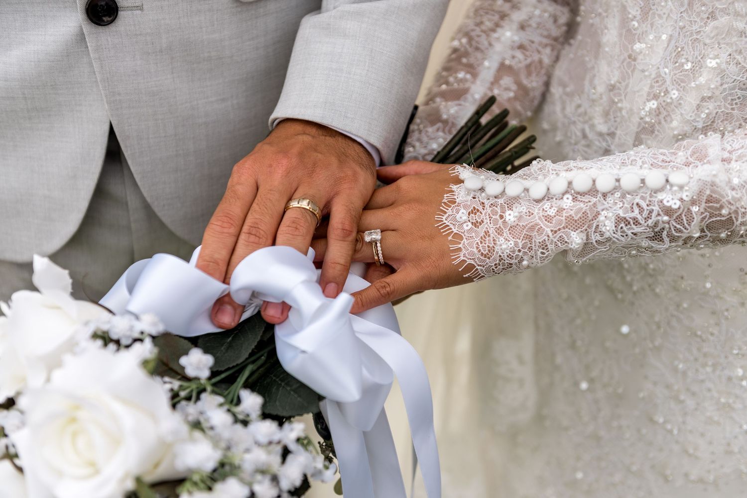 Close-up of bride and groom hands holding white bouquet with wedding rings after ceremony.