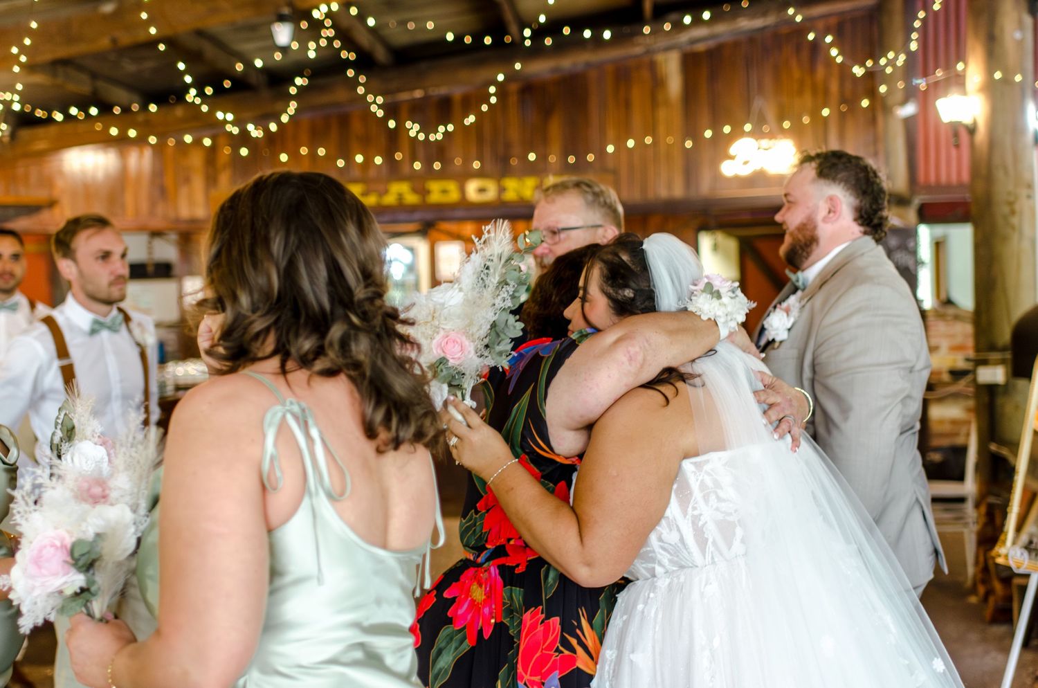Bride embraces guests under warm string lights in a rustic barn wedding reception venue.
