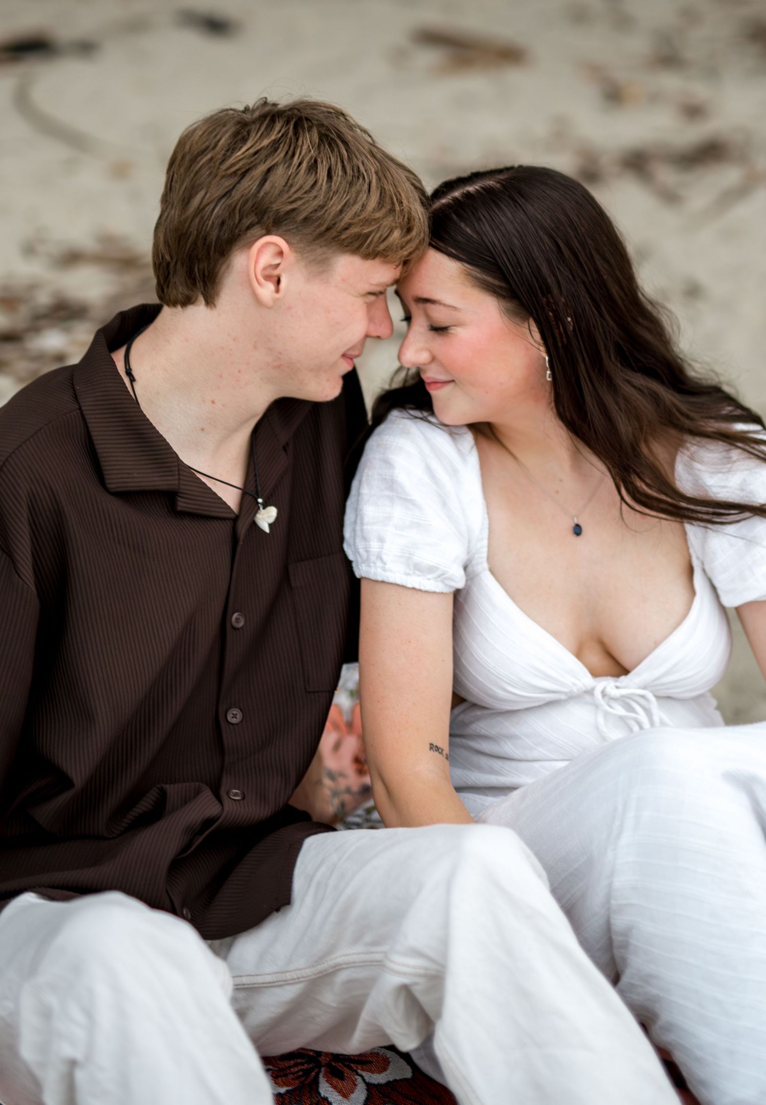 Young couple touching foreheads and holding hands in an intimate romantic moment on the beach.