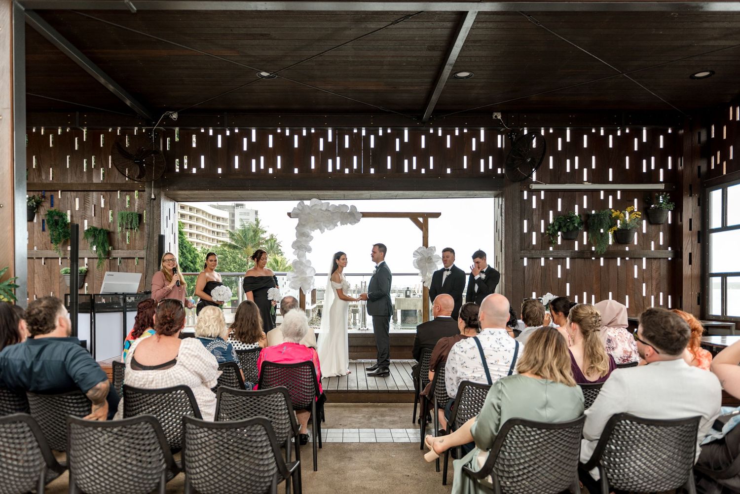 Guests seated at an intimate indoor wedding ceremony with hanging candle decor and city views.
