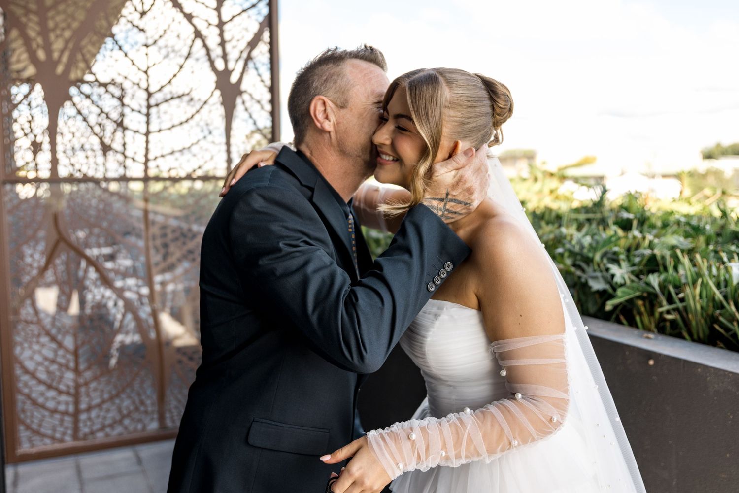 Bride and groom sharing tender kiss in wedding attire outdoors.
