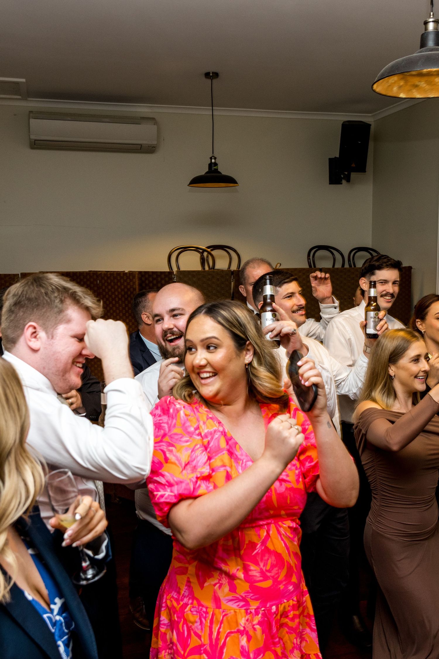 Wedding guests in formal attire dancing and celebrating joyfully at an indoor reception.