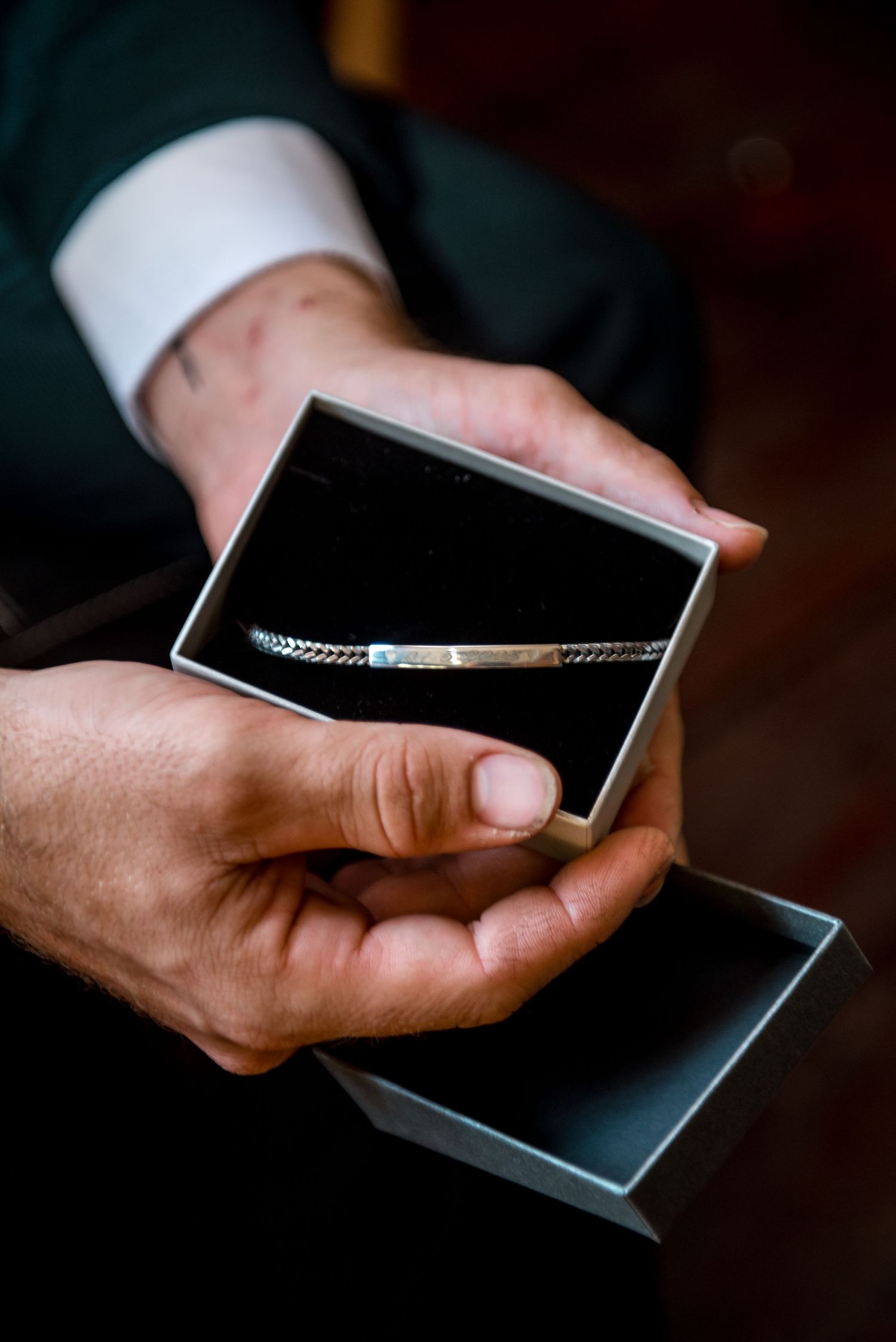 Groom holding open jewelry box with silver bracelet wedding gift.