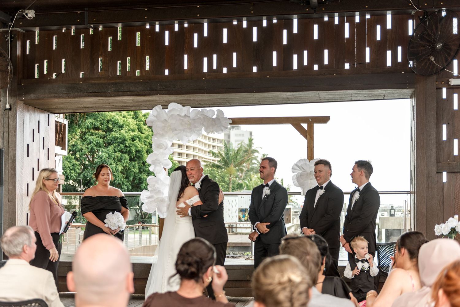 Wedding ceremony at modern open-air venue with guests seated and bridal party at altar.