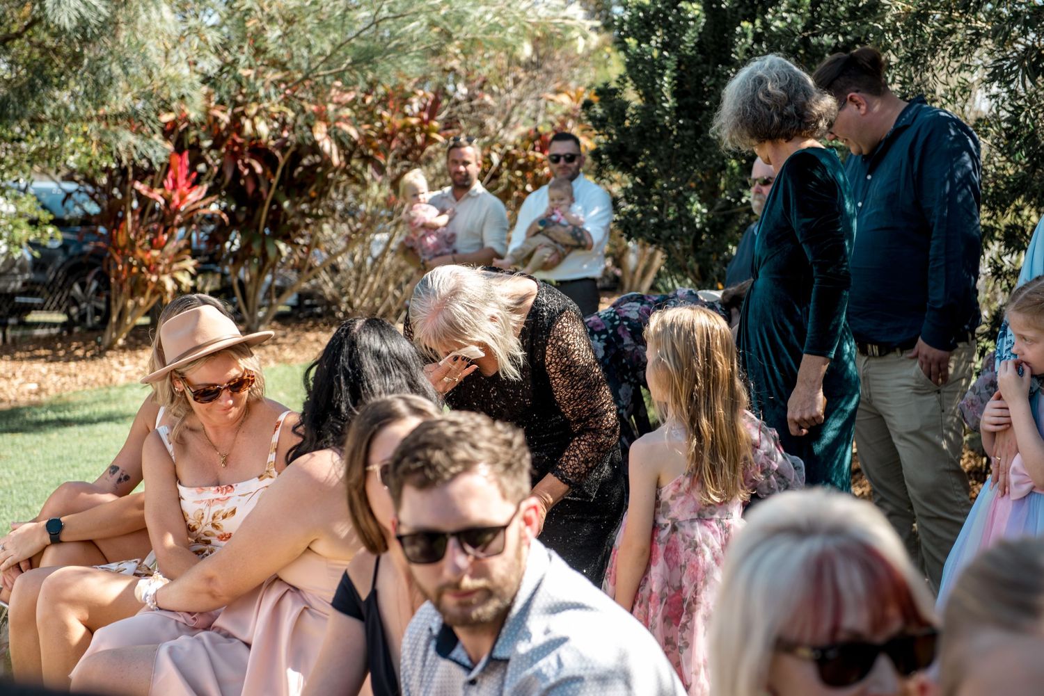 Diverse wedding guests socializing on sunny lawn, including children and adults in colorful summer attire.
