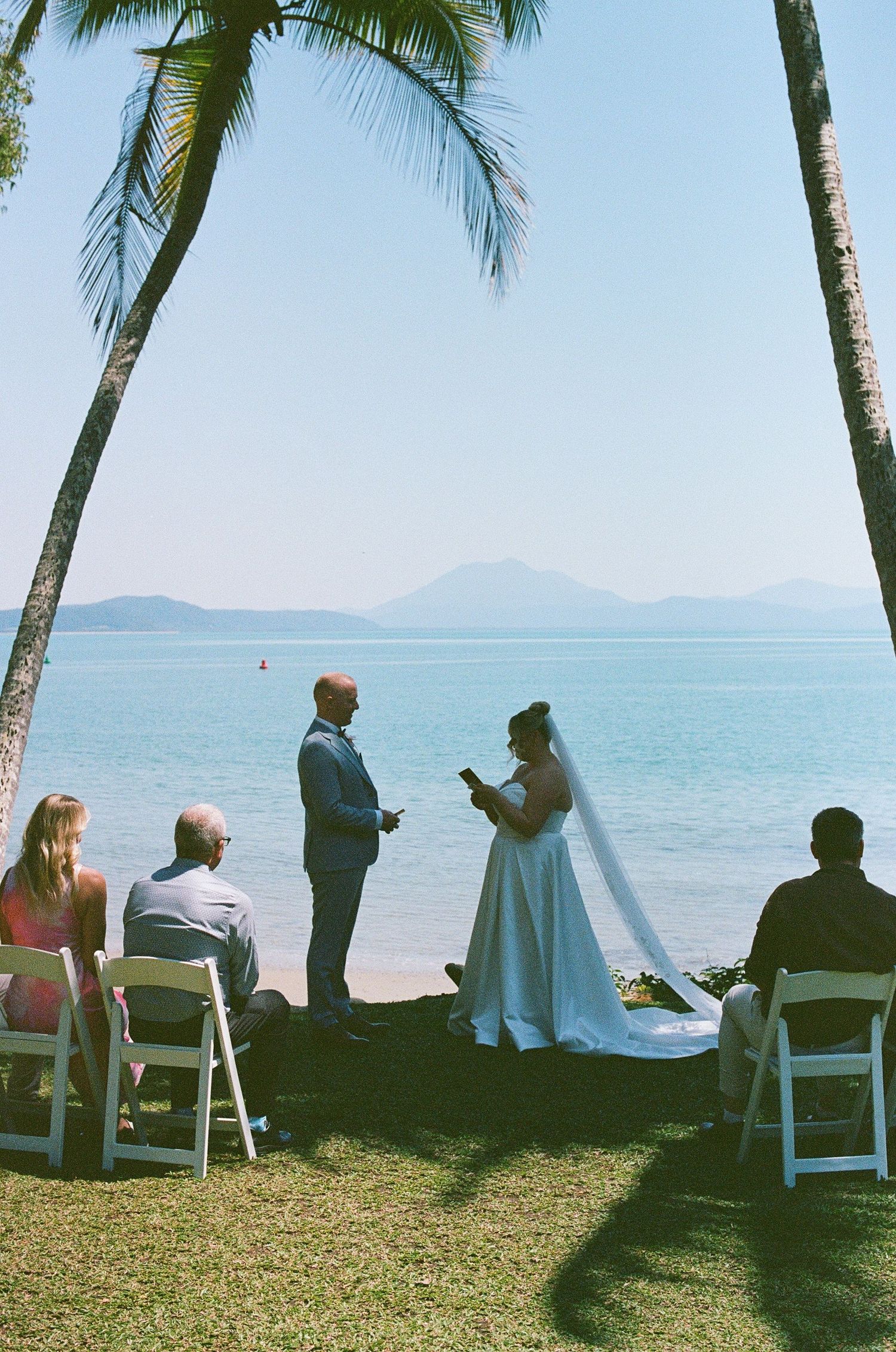 Intimate beach wedding ceremony with couple exchanging vows under palm trees by the ocean.