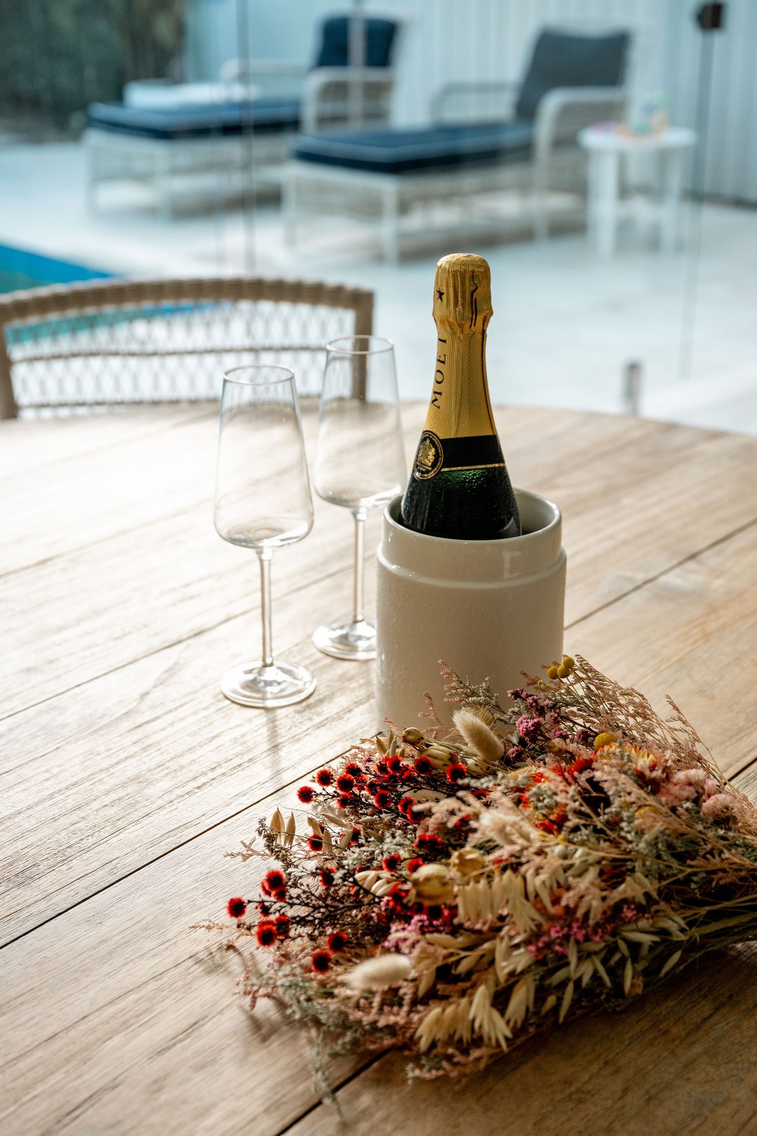 Champagne bottle in ice bucket with dried floral bouquet and glasses on wooden table at wedding reception.