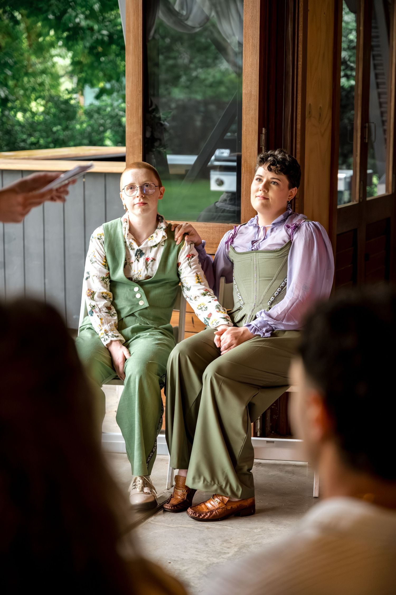 Two people in matching green outfits sit together attentively during their wedding ceremony.
