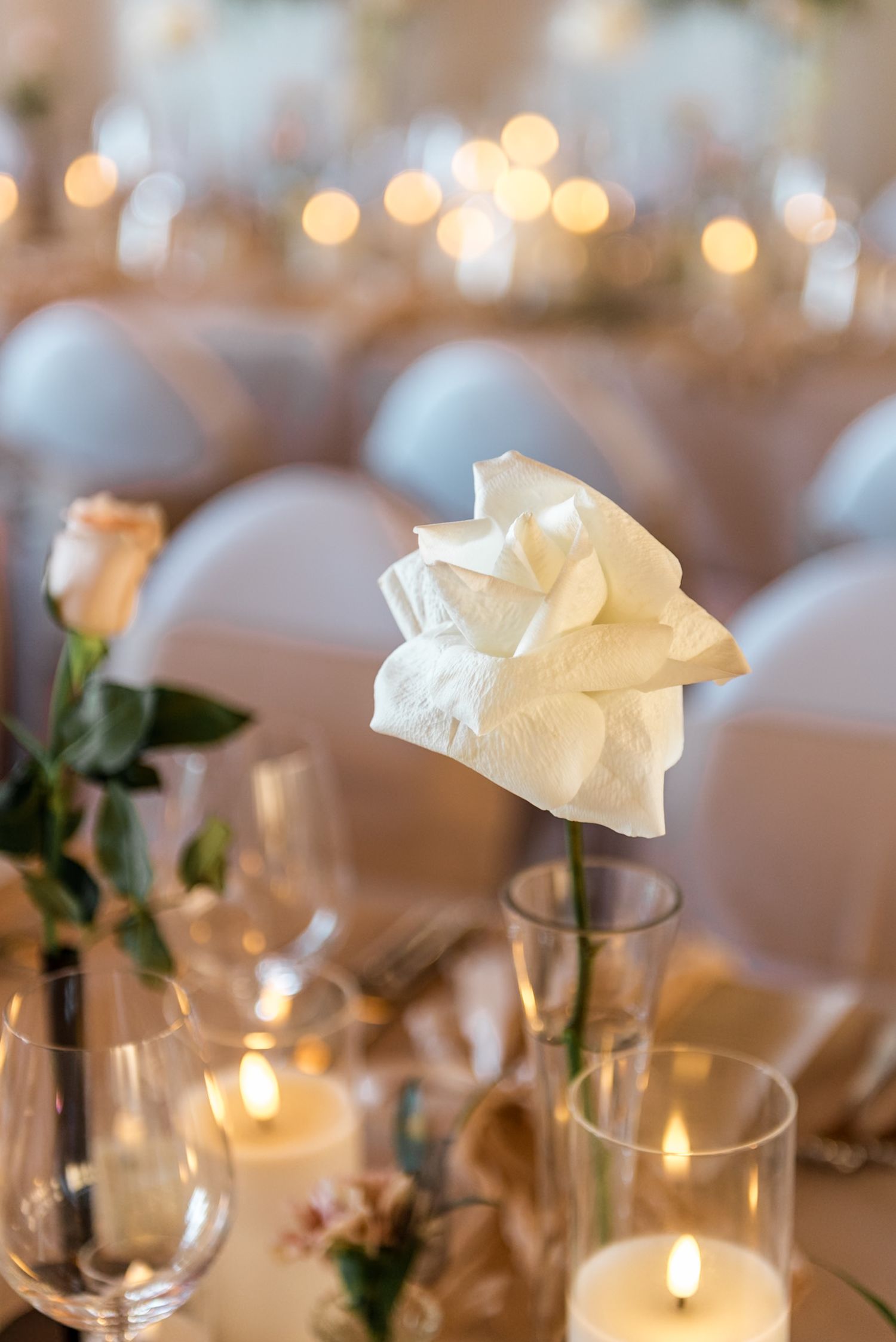 Single white rose centerpiece in glass vase surrounded by glowing candles at an elegant wedding reception.